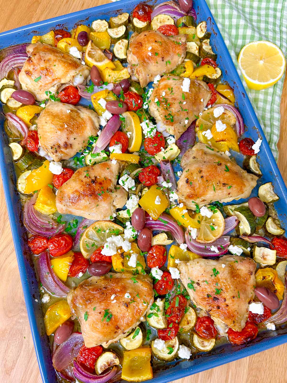 a greek sheet pan dinner is on a sheet pan with chicken thighs, roasted vegetables and feta cheese