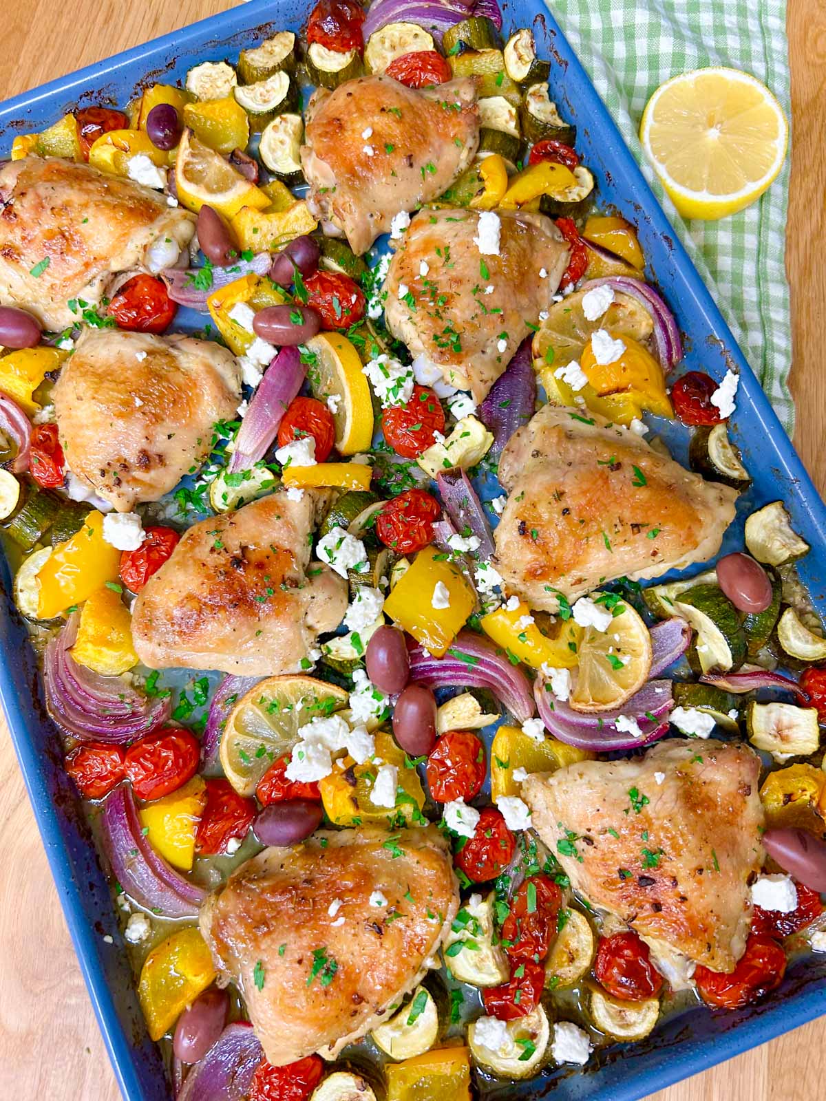 a greek sheet pan dinner is on a sheet pan with chicken thighs, roasted vegetables and feta cheese