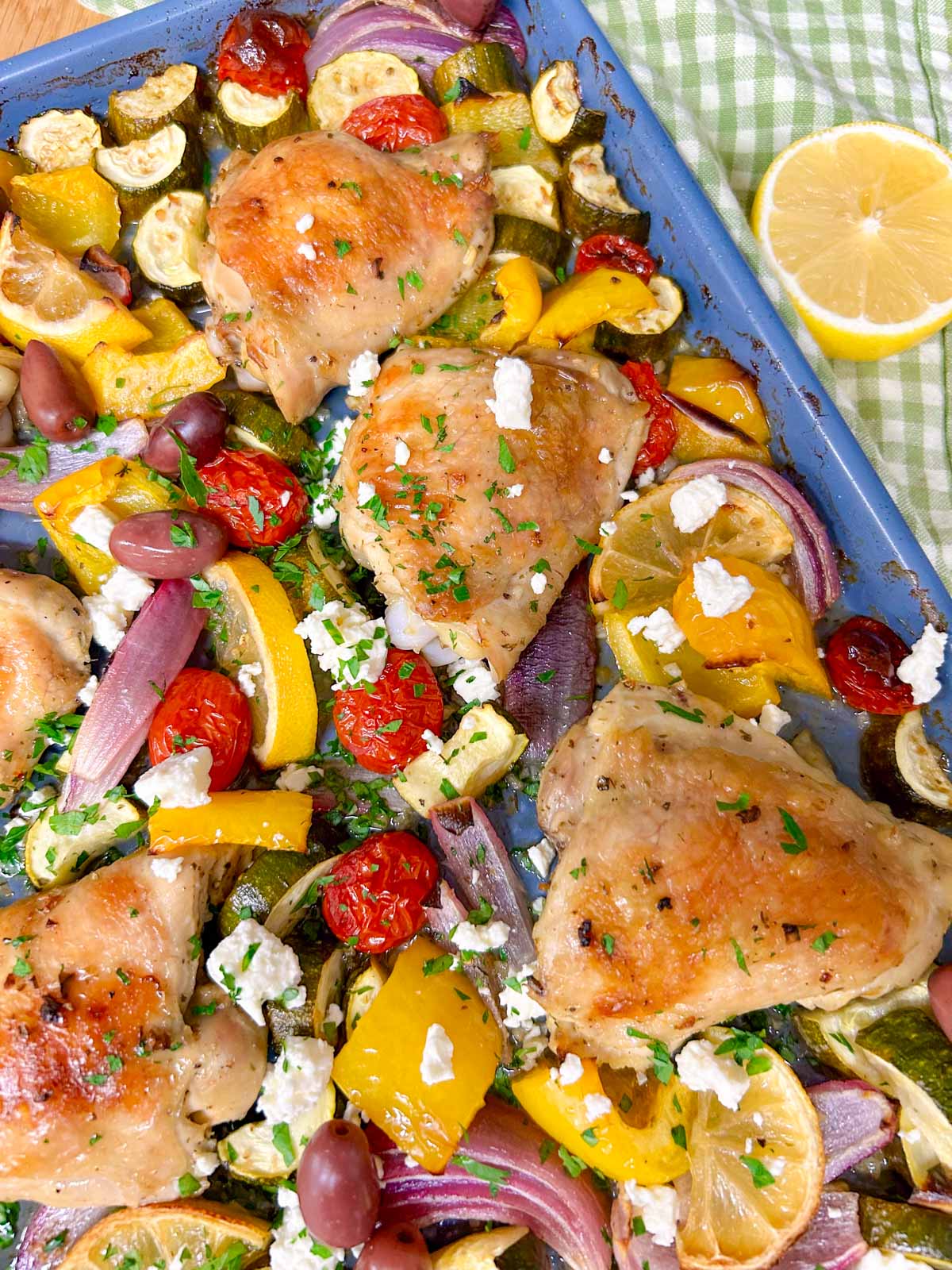 a greek sheet pan dinner is on a sheet pan with chicken thighs, roasted vegetables and feta cheese