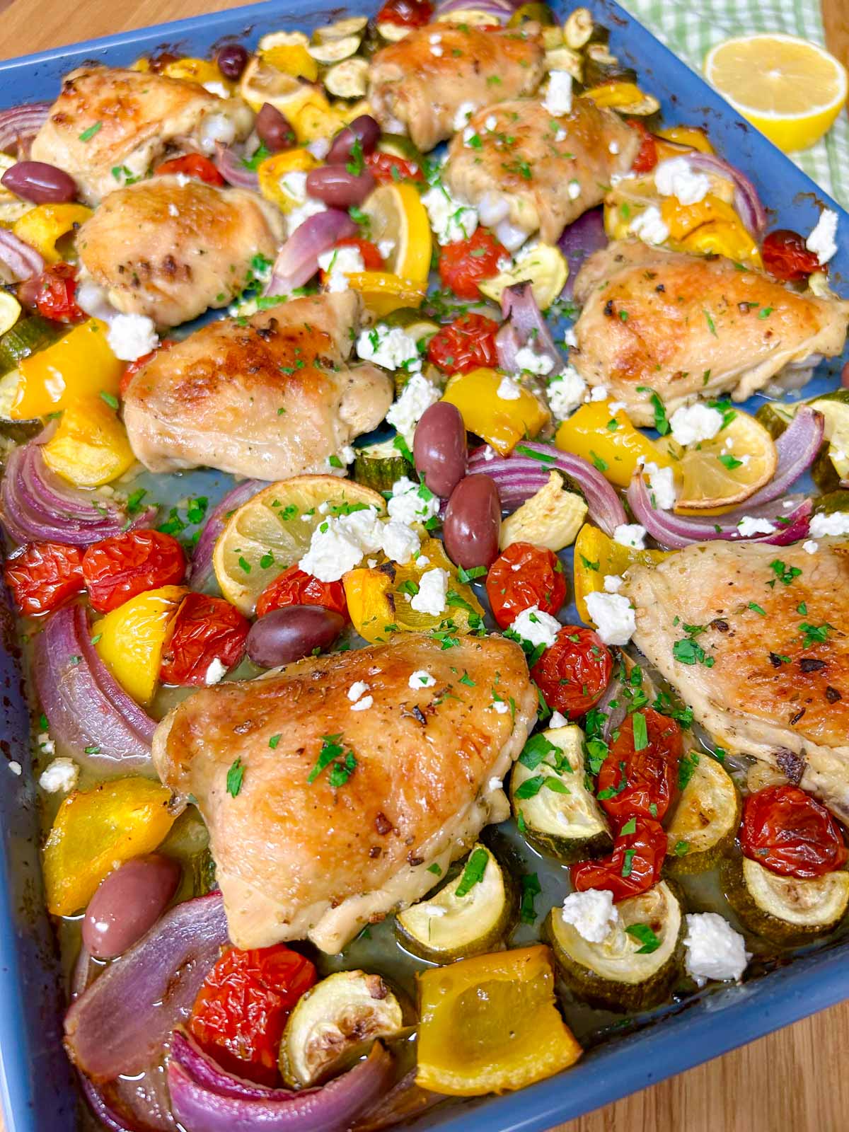 a greek sheet pan dinner is on a sheet pan with chicken thighs, roasted vegetables and feta cheese
