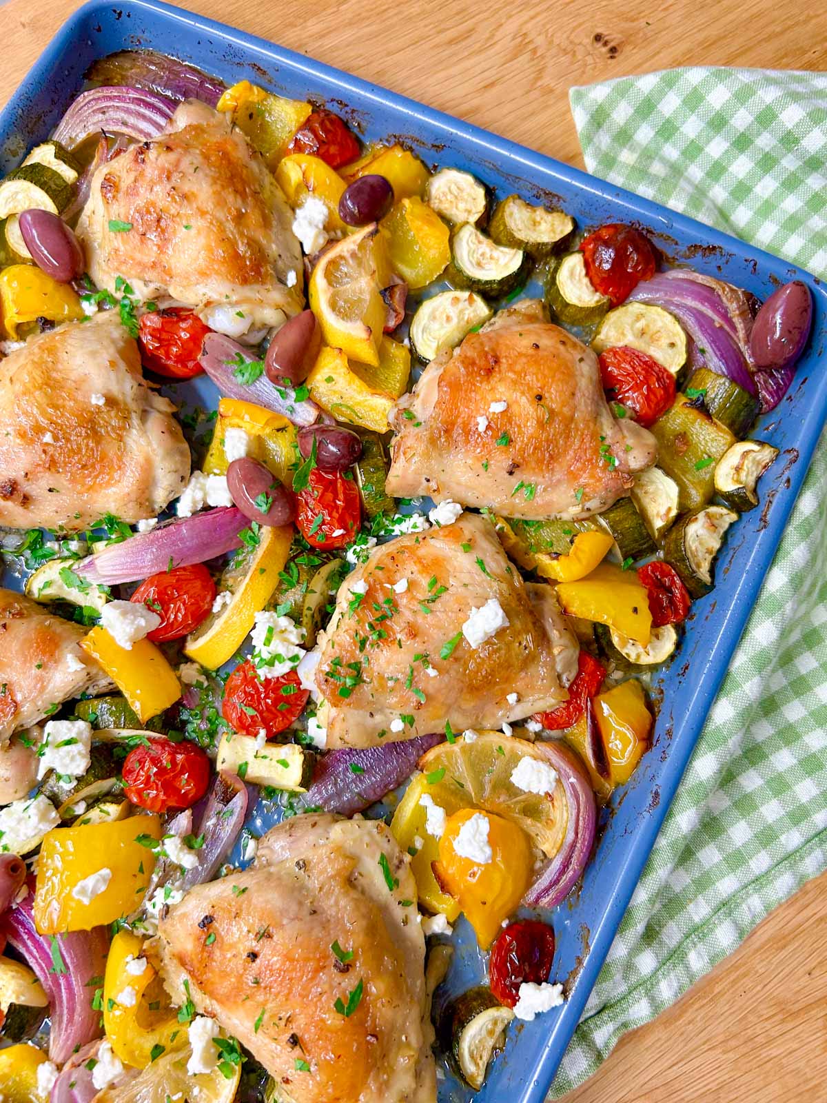 a greek sheet pan dinner is on a sheet pan with chicken thighs, roasted vegetables and feta cheese