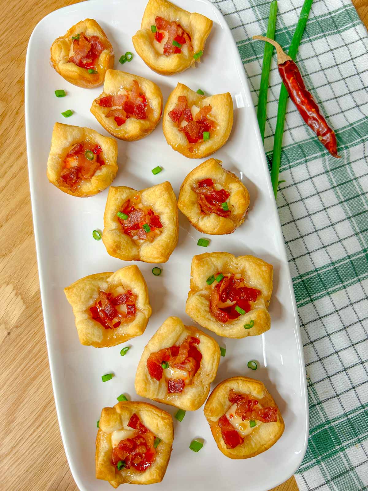 a white platter has bacon pepper jelly cheese cups garnished with green onions