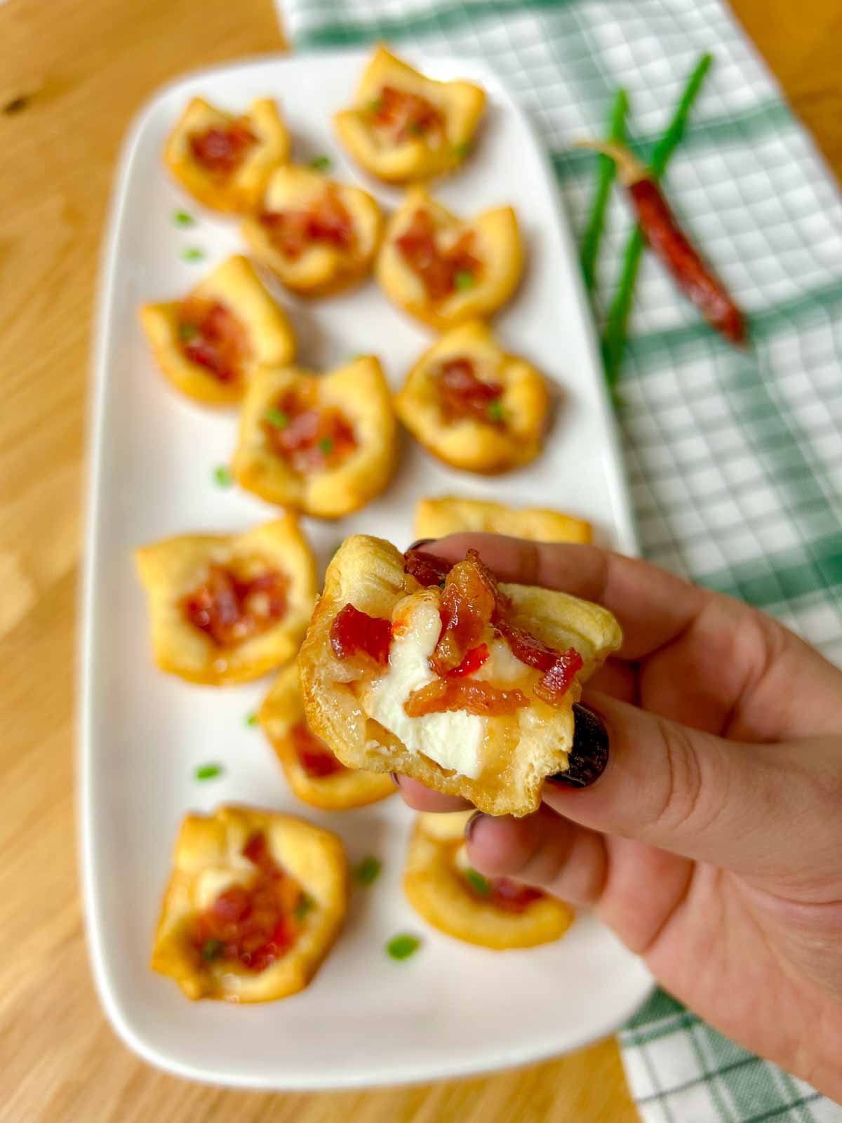 a white platter has bacon pepper jelly cheese cups garnished with green onions. one is bit in half and held close to the camera