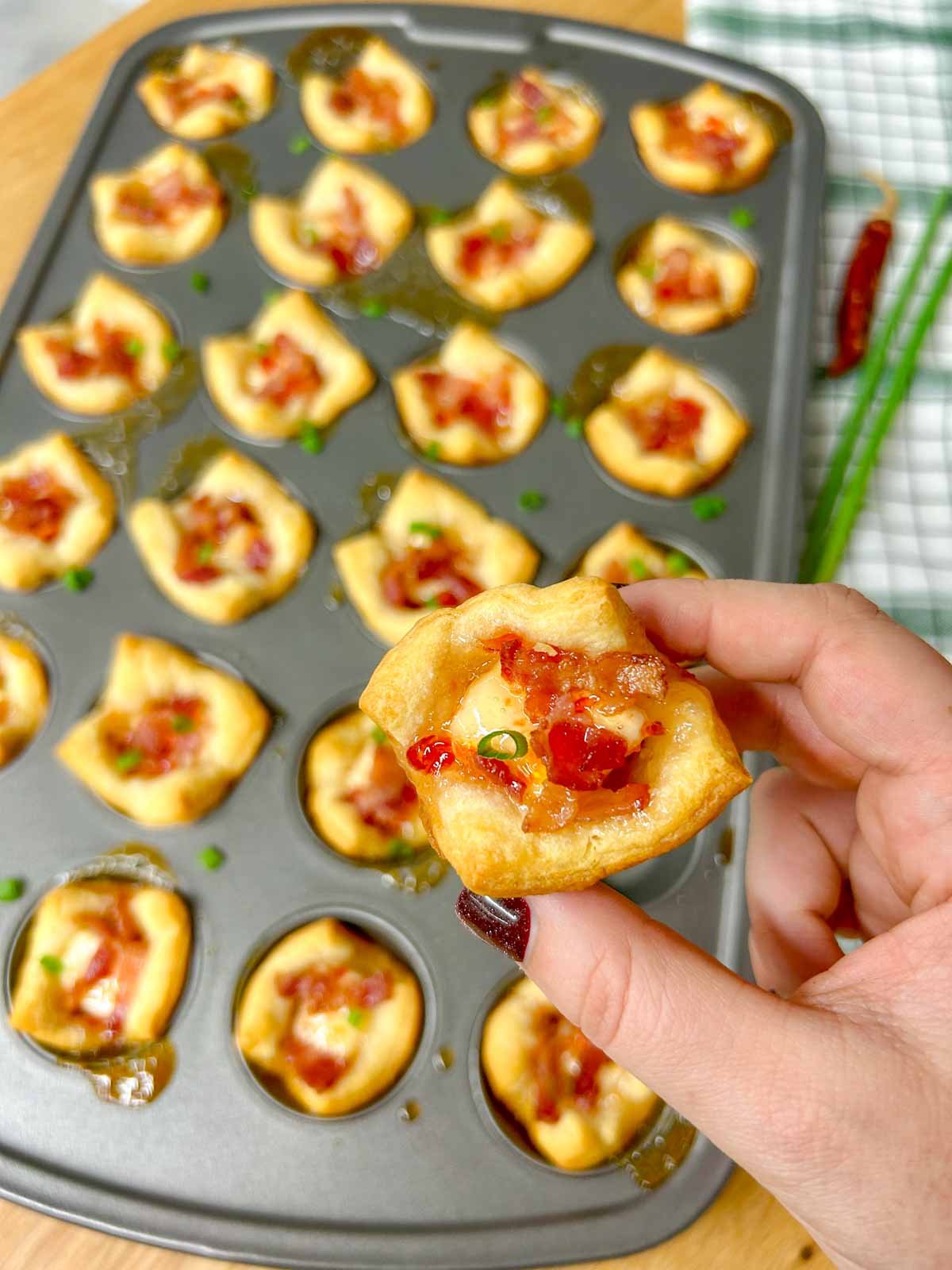 mini muffin tin with the bacon pepper jelly cheese cups. one is held up close to camera.