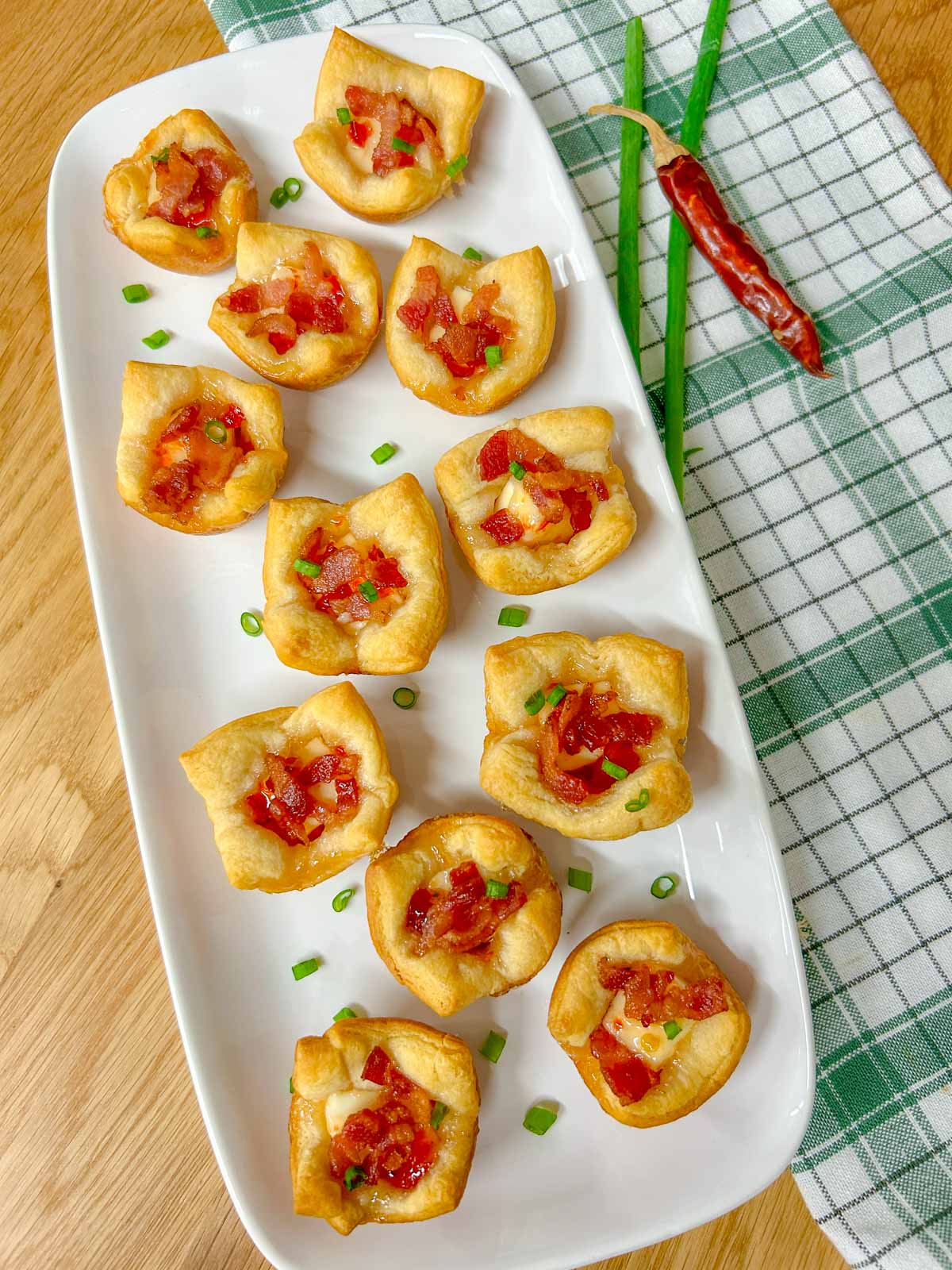 a white platter has bacon pepper jelly cheese cups garnished with green onions