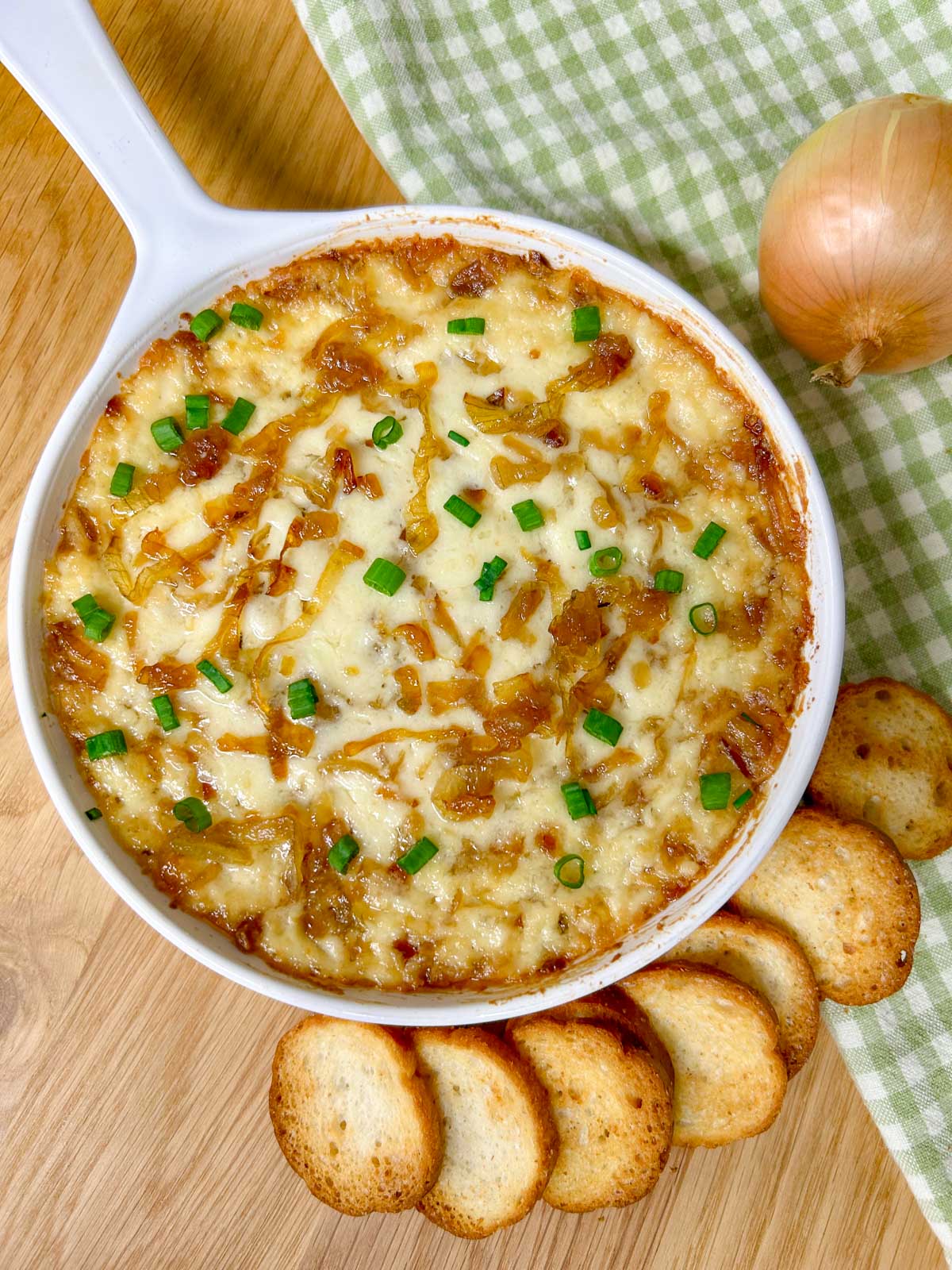 a white dish is filled with baked caramelized onion dip and garnished with green onions