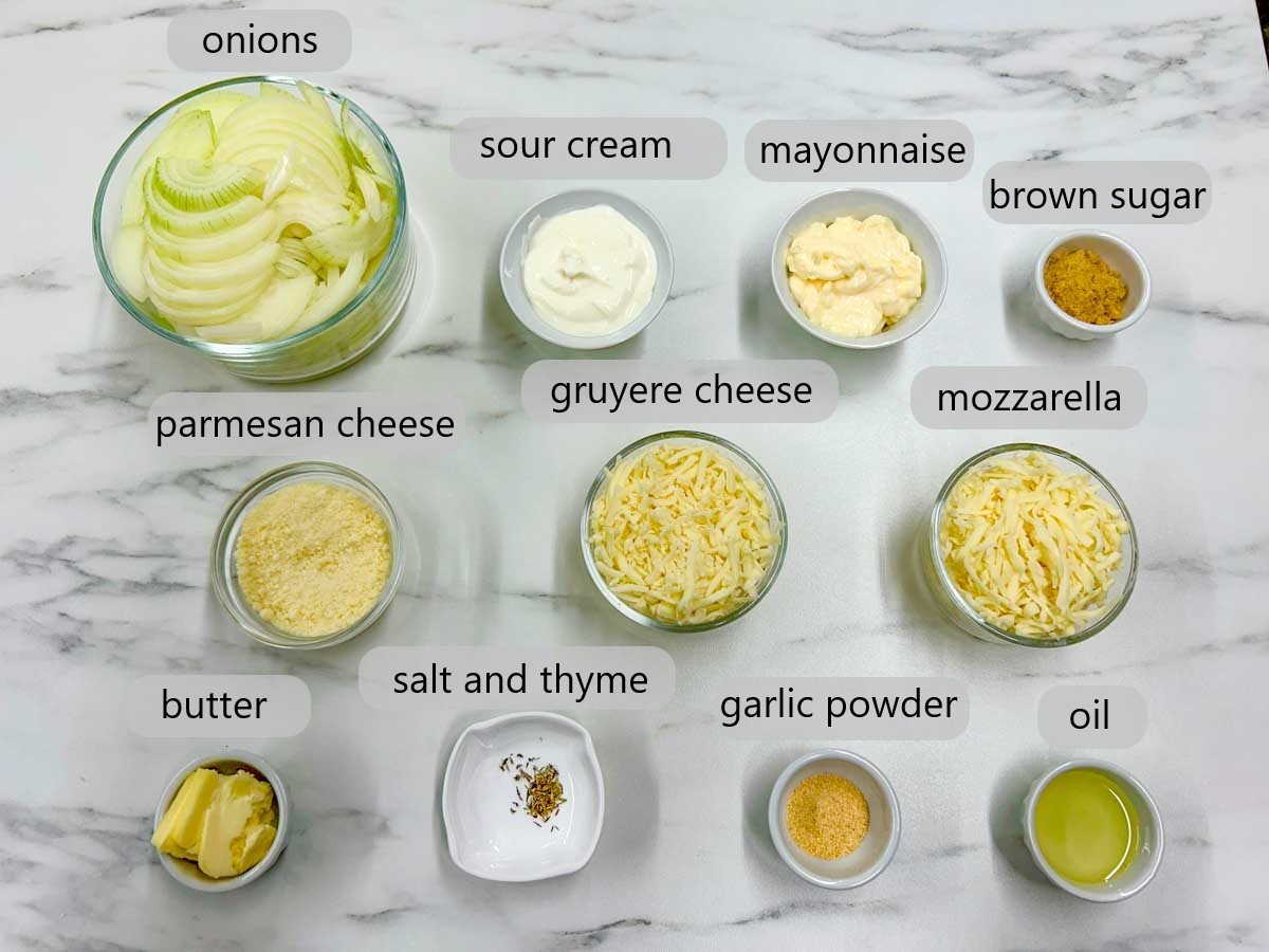a counter to with bowls and ingredient labels reading onions, sour cream, mayonnaise, brown sugar, parmesan cheese, gruyere cheese, mozzarella, butter, salt and thyme, garlic powder and oil.
