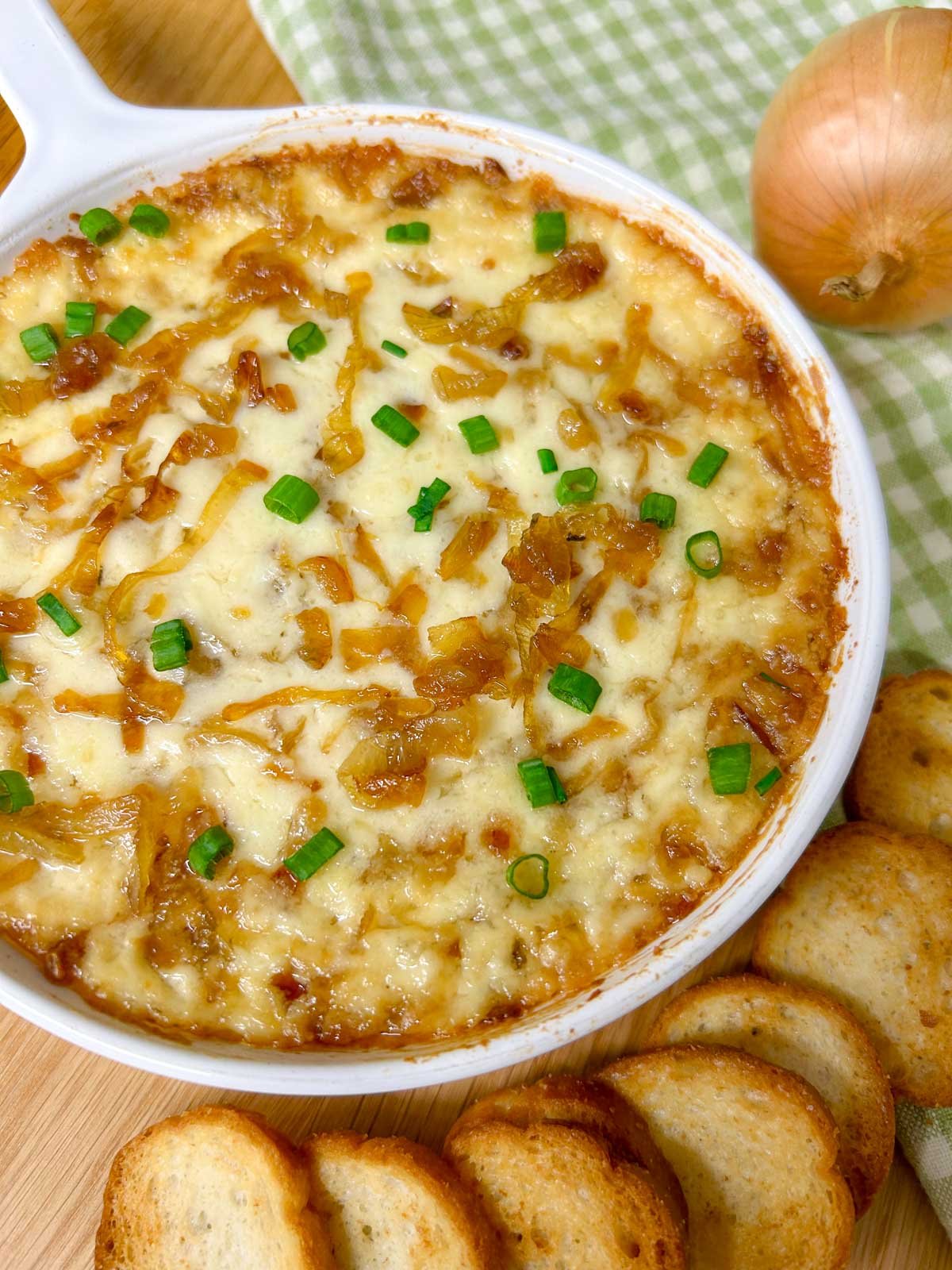 a white dish is filled with baked caramelized onion dip and garnished with green onions