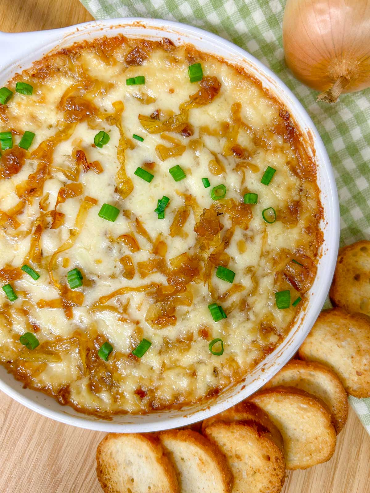 a white dish is filled with baked caramelized onion dip and garnished with green onions