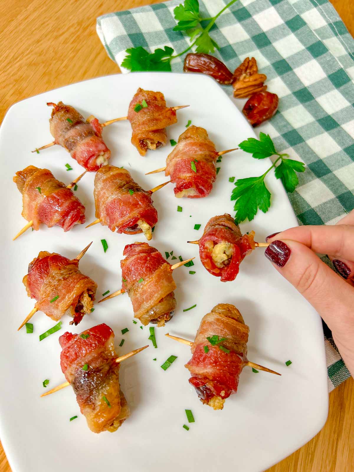 a white plate had boursin stuffed bacon wrapped dates on it and garnished with chopped parsley. one is held up close to the camera