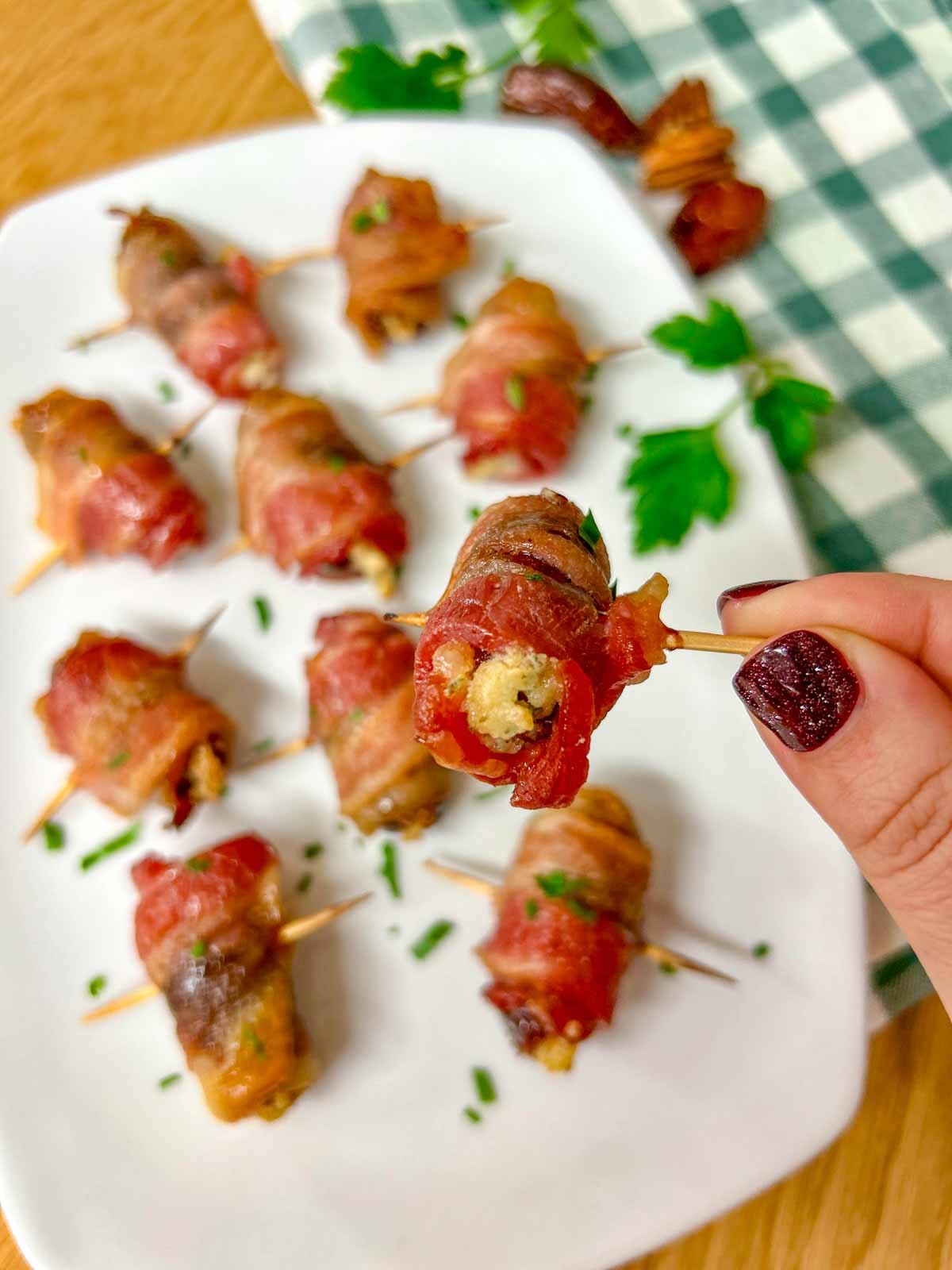 a white plate had boursin stuffed bacon wrapped dates on it and garnished with chopped parsley.