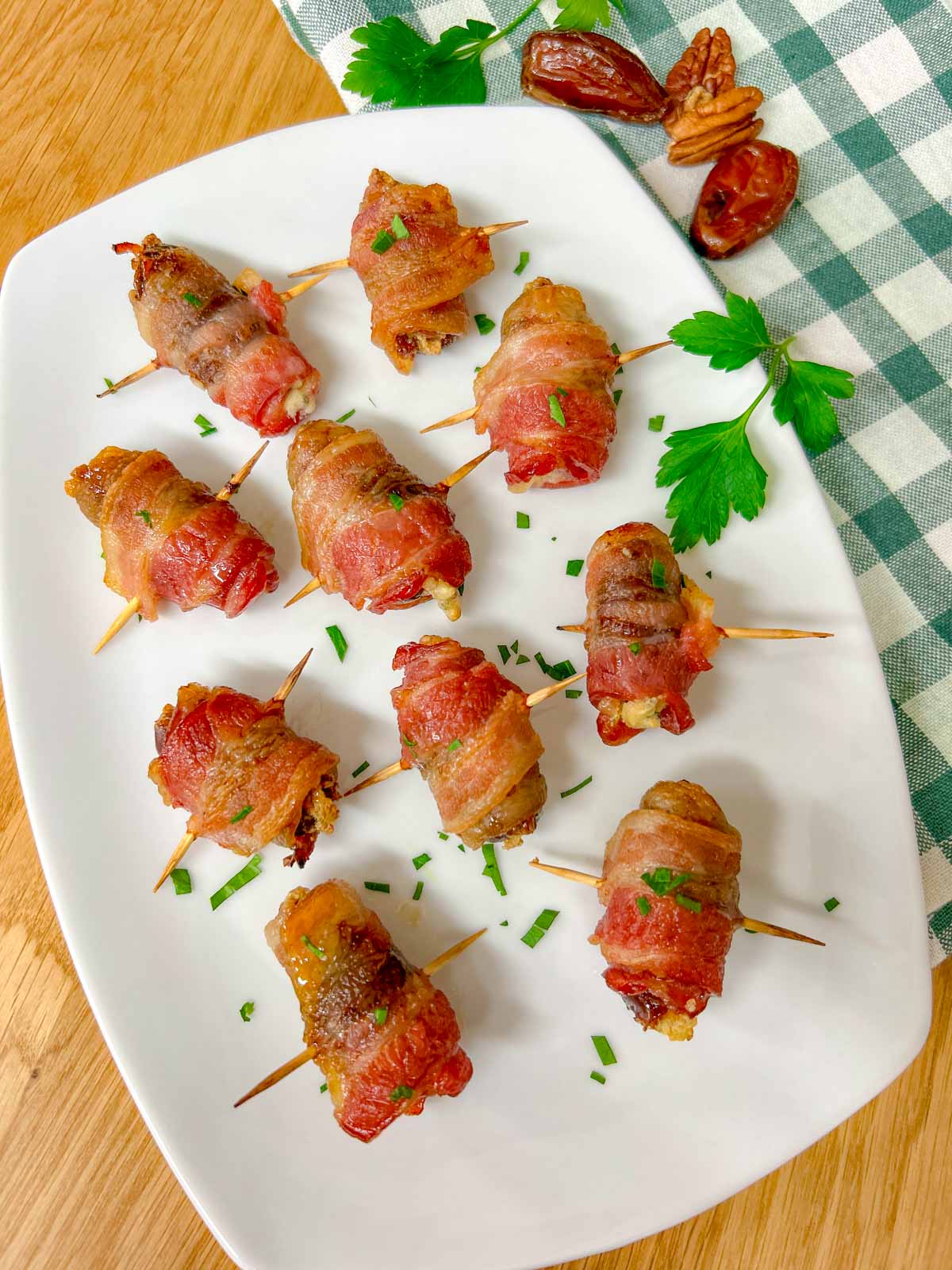 a white plate had boursin stuffed bacon wrapped dates on it and garnished with chopped parsley.