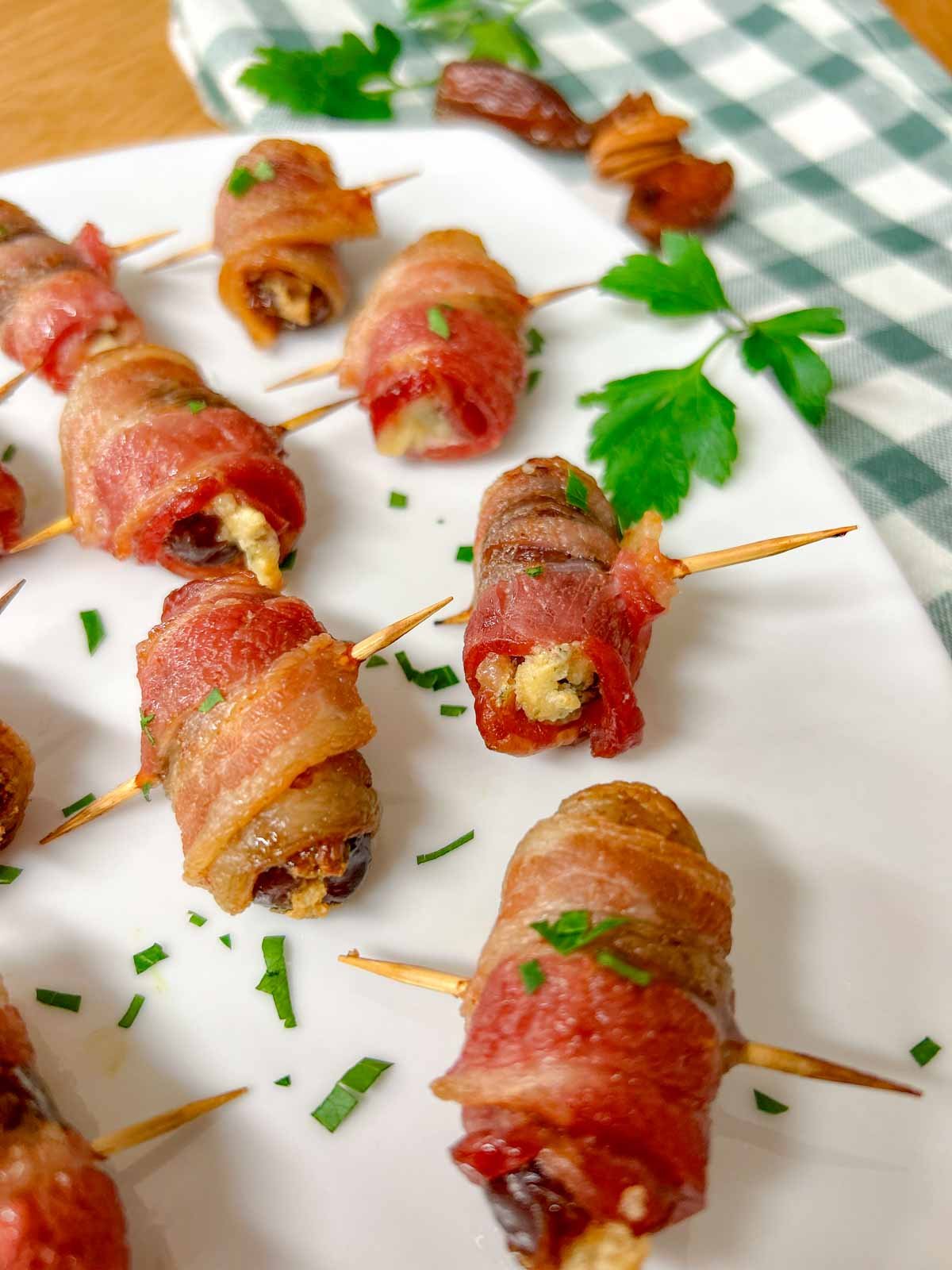 a white plate had boursin stuffed bacon wrapped dates on it and garnished with chopped parsley.