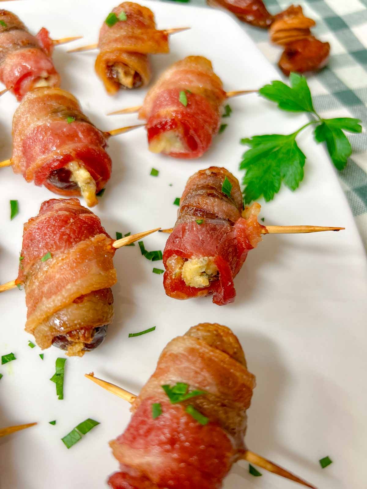 a white plate had boursin stuffed bacon wrapped dates on it and garnished with chopped parsley.