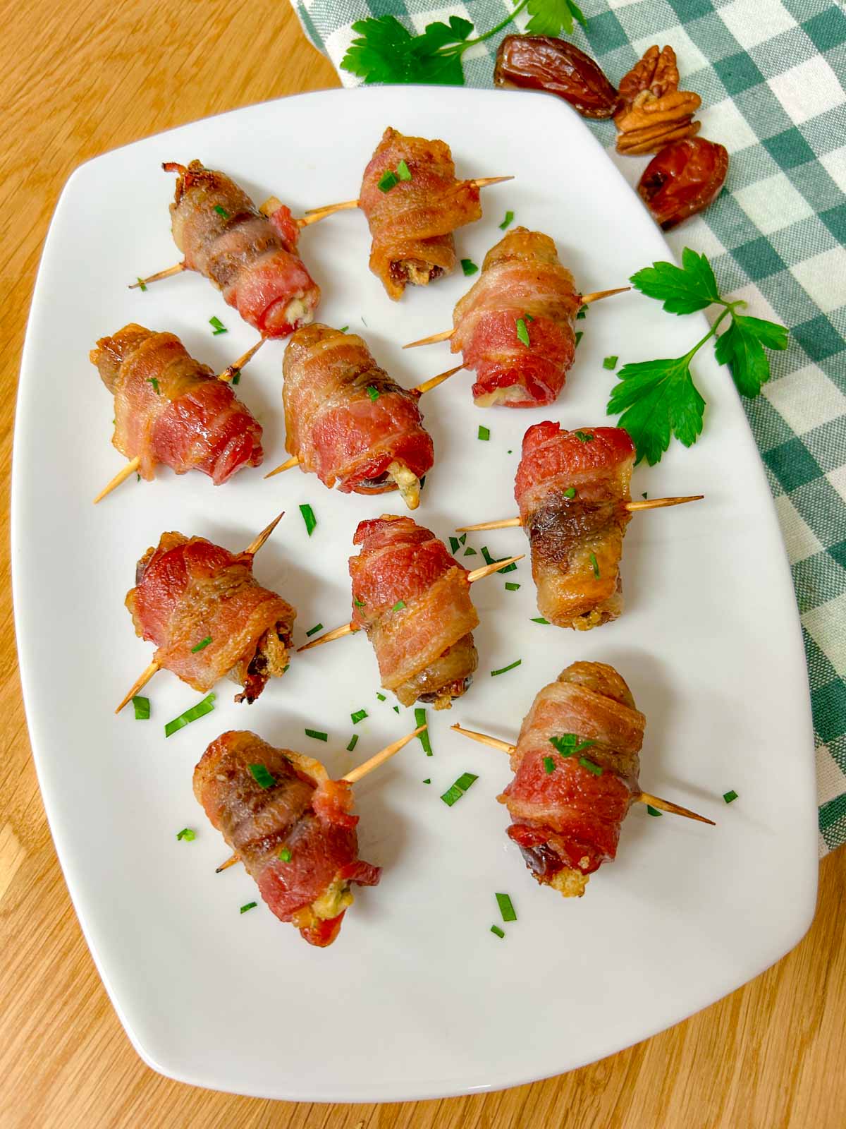 a white plate had boursin stuffed bacon wrapped dates on it and garnished with chopped parsley.
