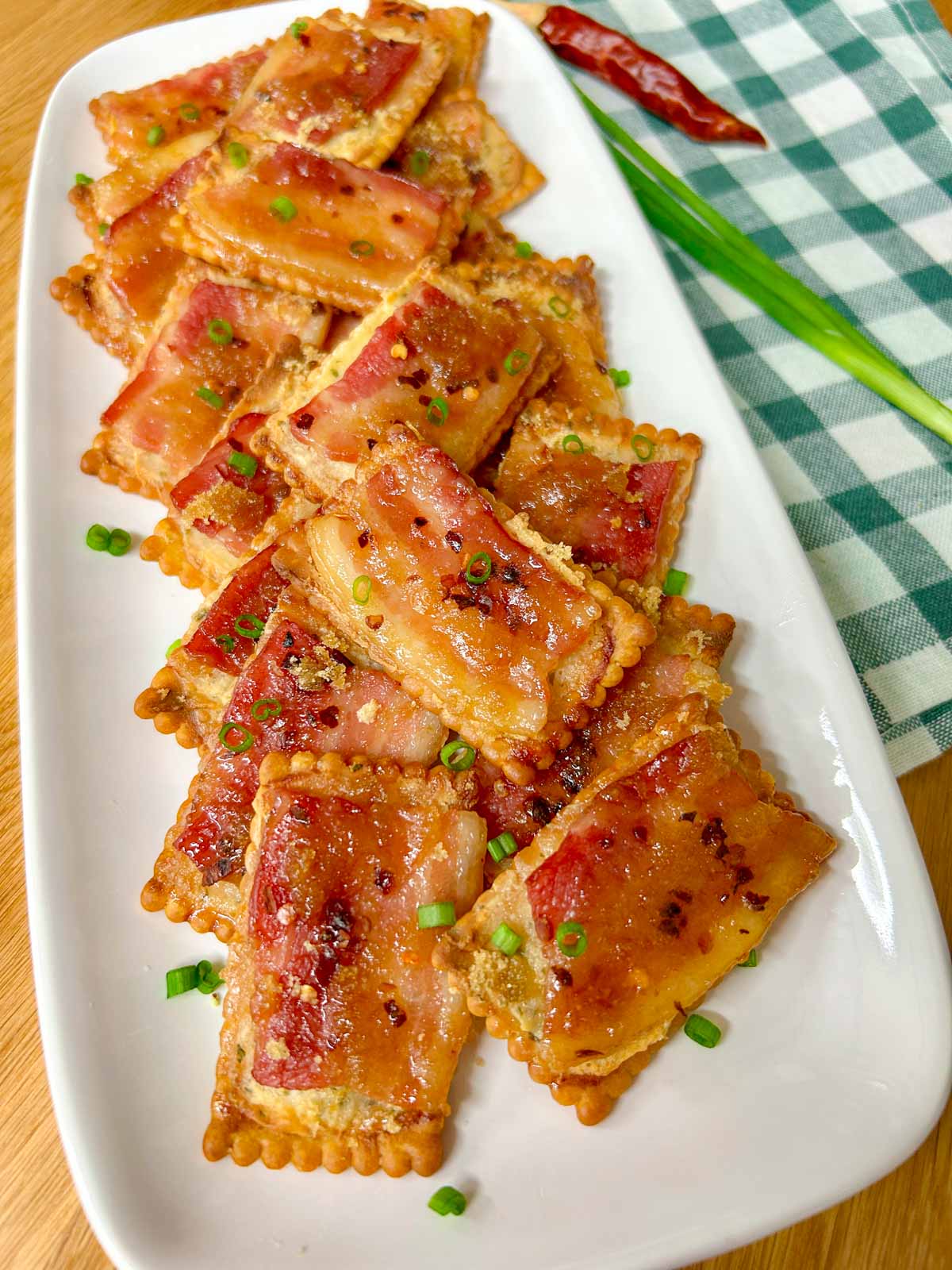 a white plate has candied bacon boursin crackers on top and garnished with green onions