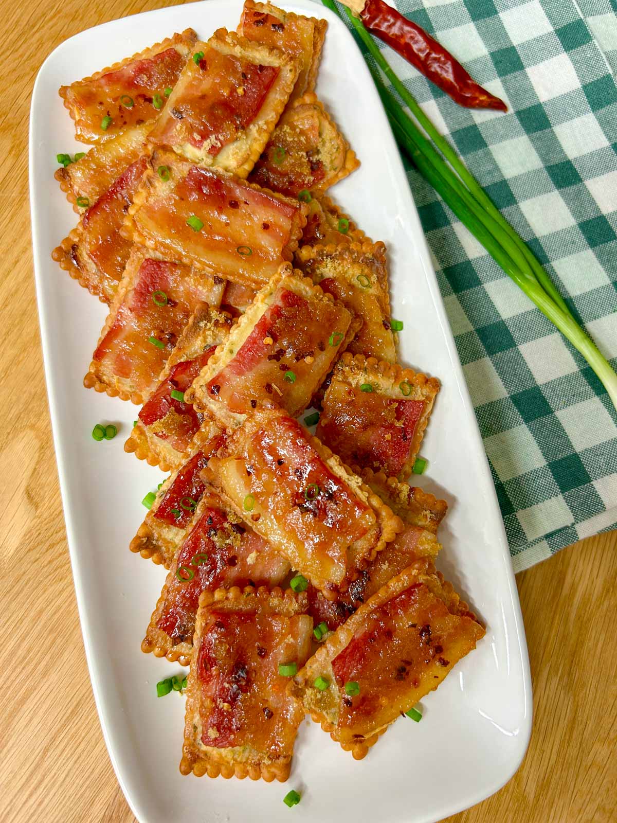 a white plate has candied bacon boursin crackers on top and garnished with green onions