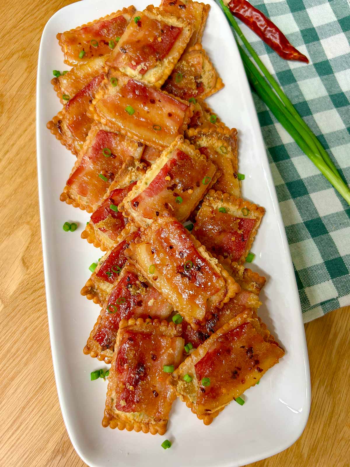 a white plate has candied bacon boursin crackers on top and garnished with green onions