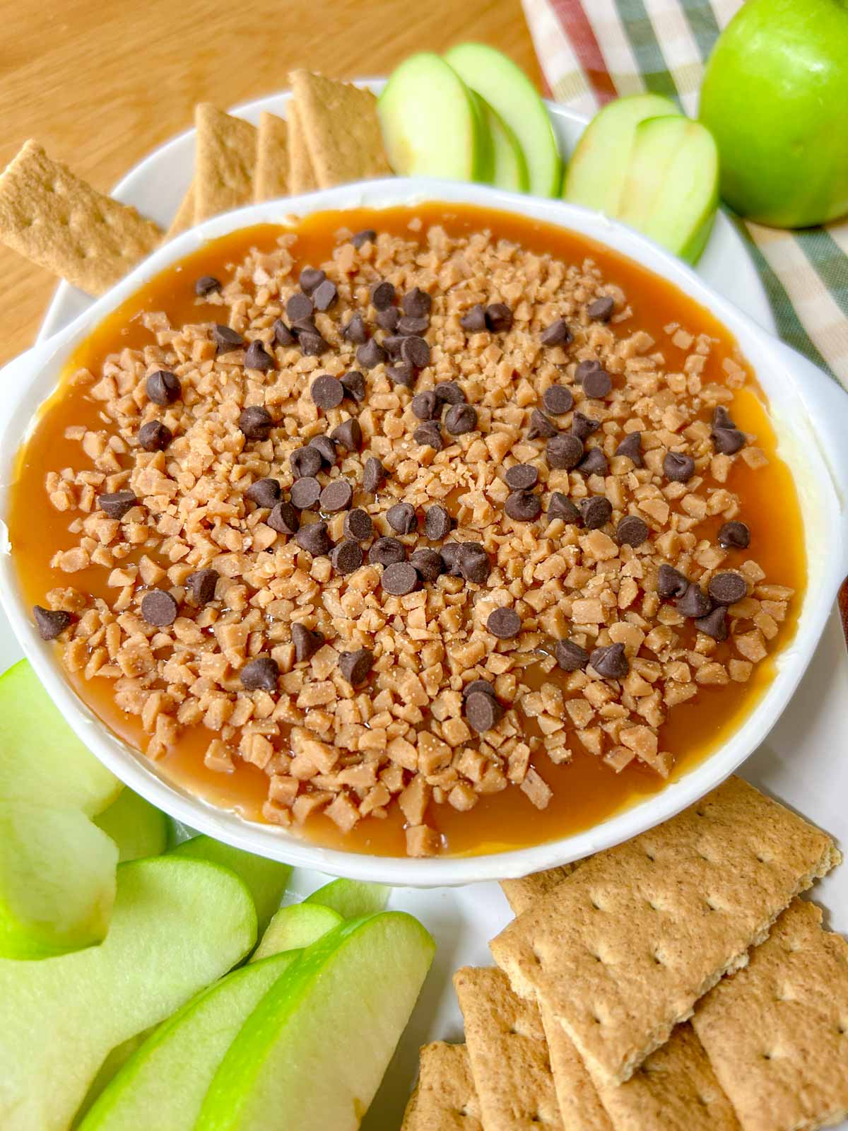 a white bowl is filled with caramel apple cheesecake dip and served with apple and graham crackers to dip