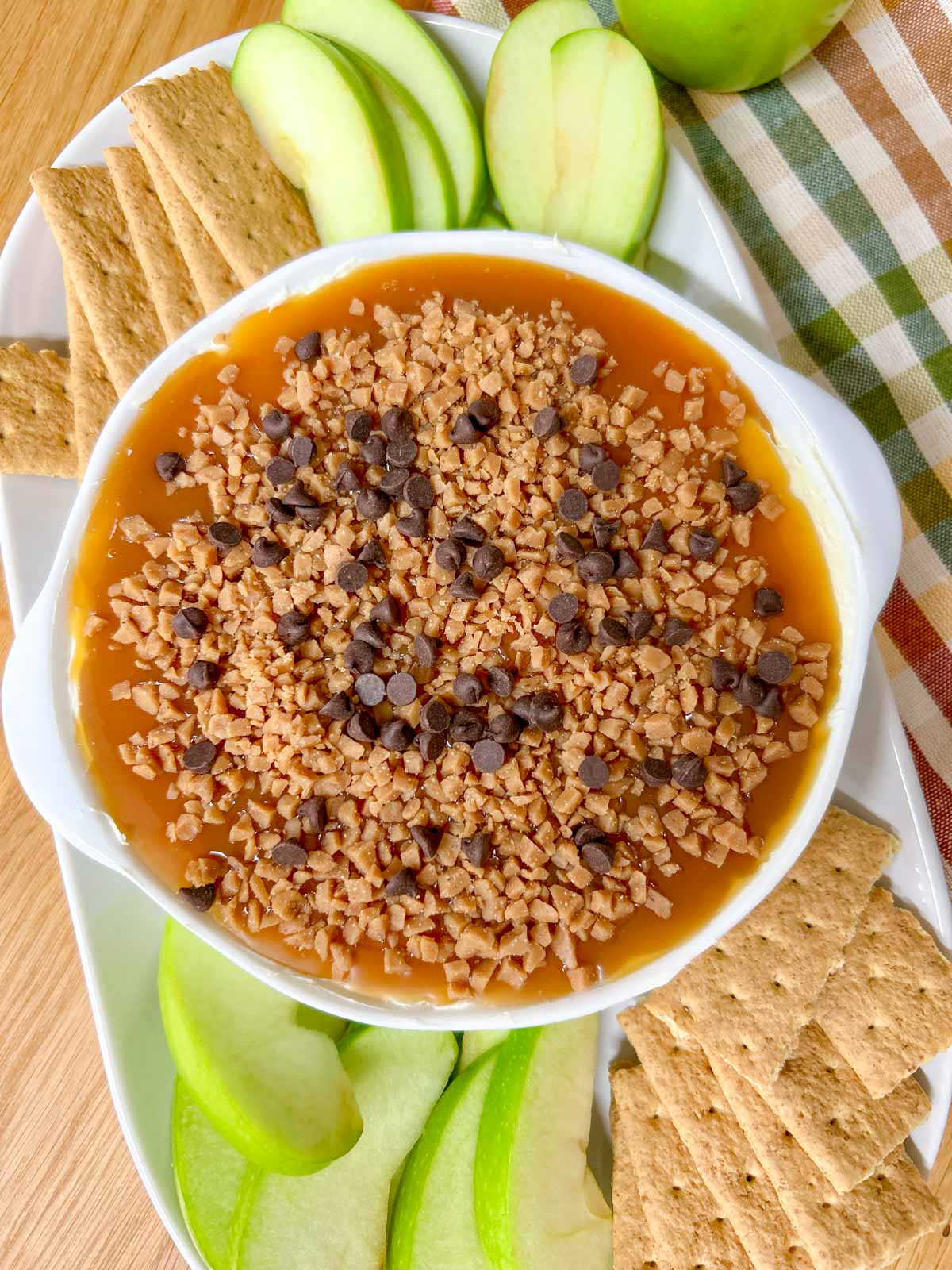 a white bowl is filled with caramel apple cheesecake dip and served with apple and graham crackers to dip