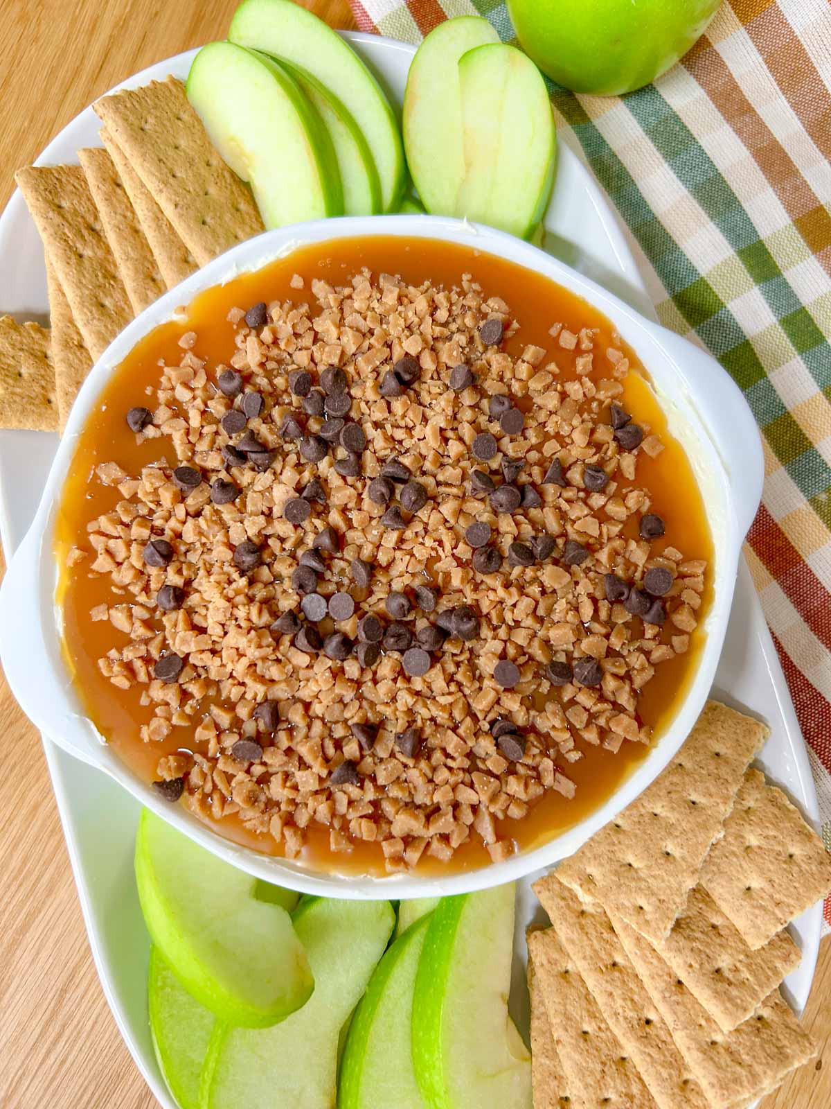 a white bowl is filled with caramel apple cheesecake dip and served with apple and graham crackers to dip