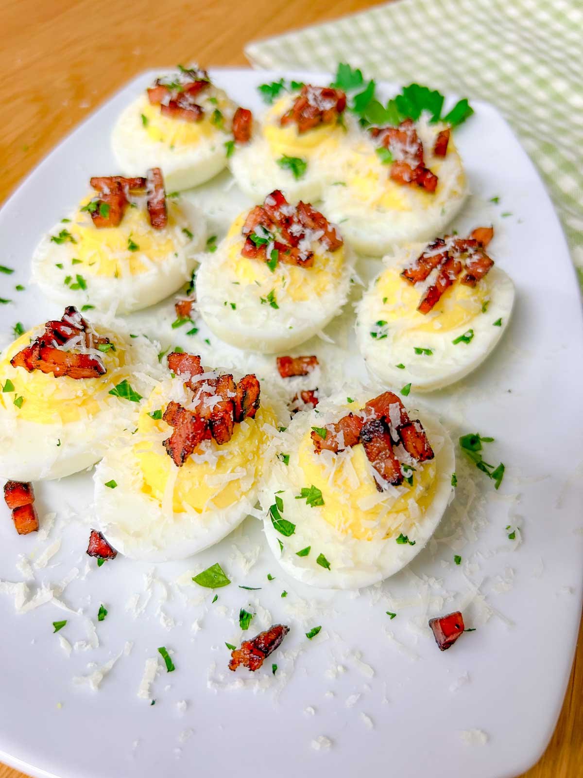 a white serving platter is filled with carbonara deviled eggs that are topped with crispy pancetta, grated parmesan cheese, and fresh parsley