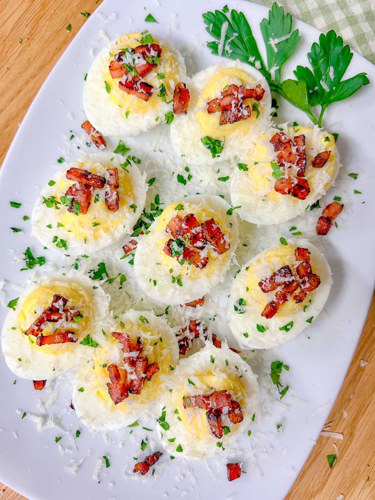a white serving platter is filled with carbonara deviled eggs that are topped with crispy pancetta, grated parmesan cheese, and fresh parsley