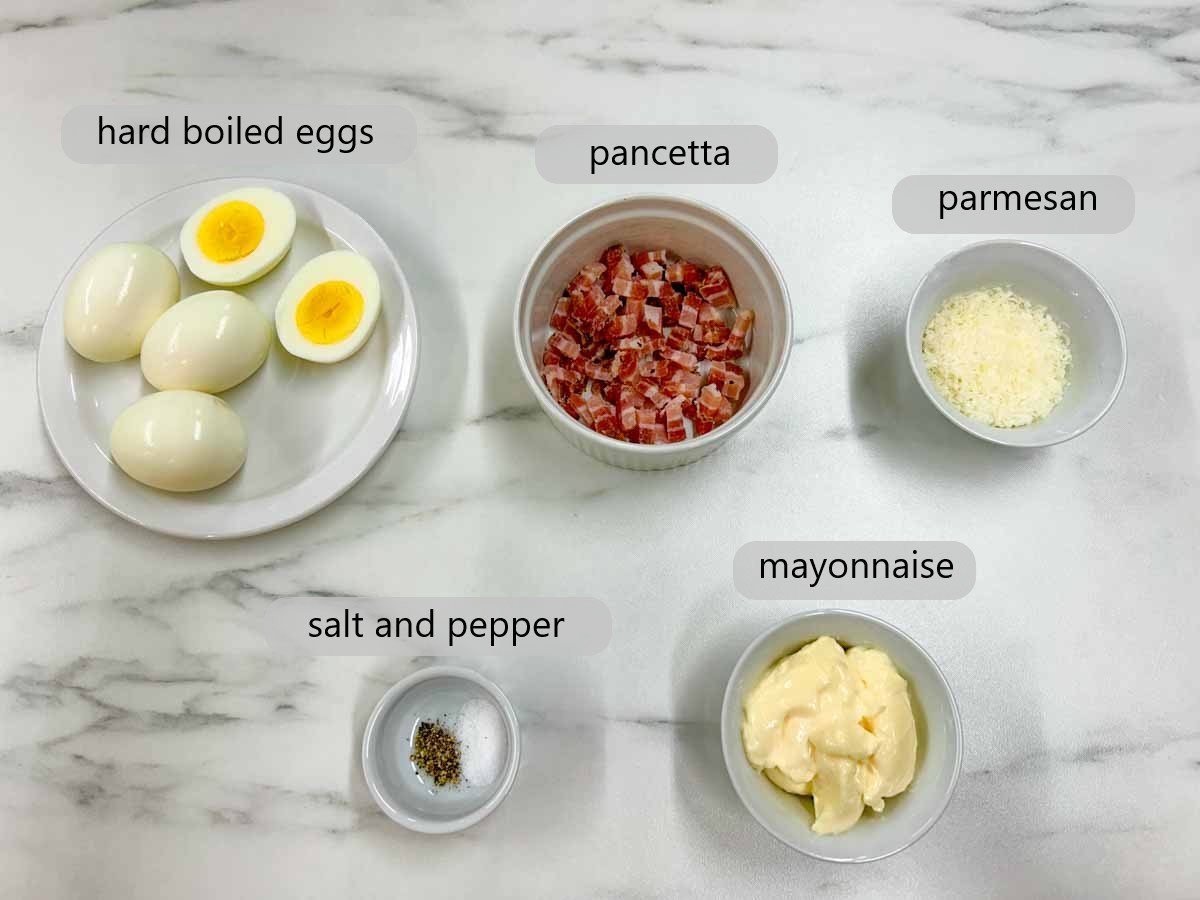 kitchen counter top with the ingredients to make carbonara deviled eggs and text overlays reading hard boiled eggs, pancetta, salt and pepper, mayonnaise