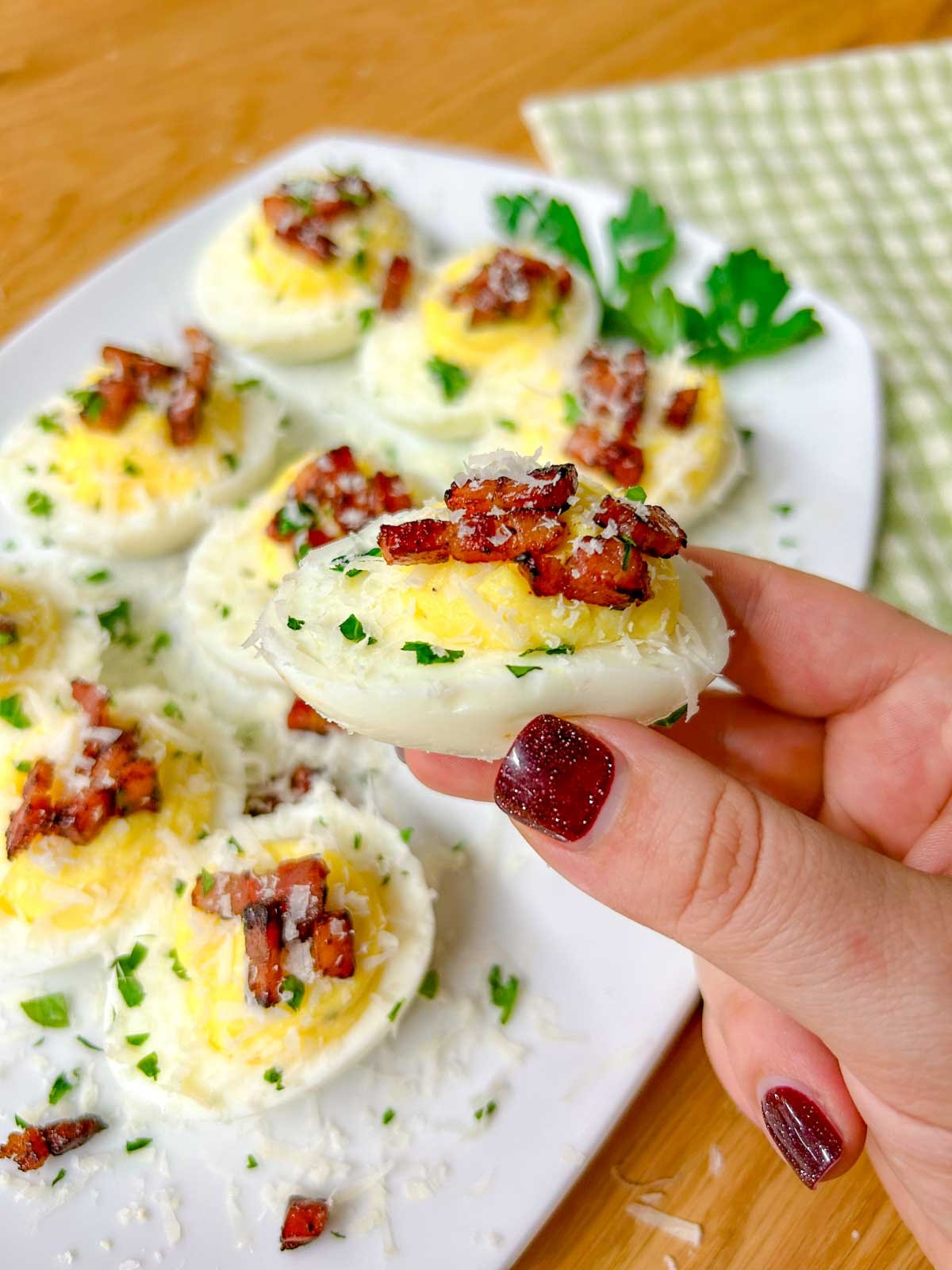 a white serving platter is filled with carbonara deviled eggs that are topped with crispy pancetta, grated parmesan cheese, and fresh parsley