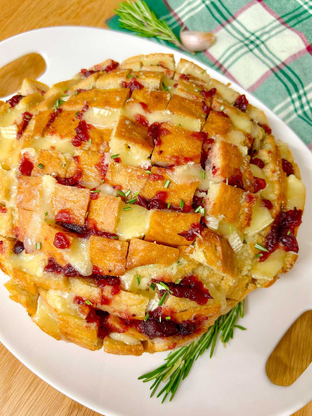 a loaf of cranberry brie pull apart garlic bread it on a white platter and garnished with rosemary