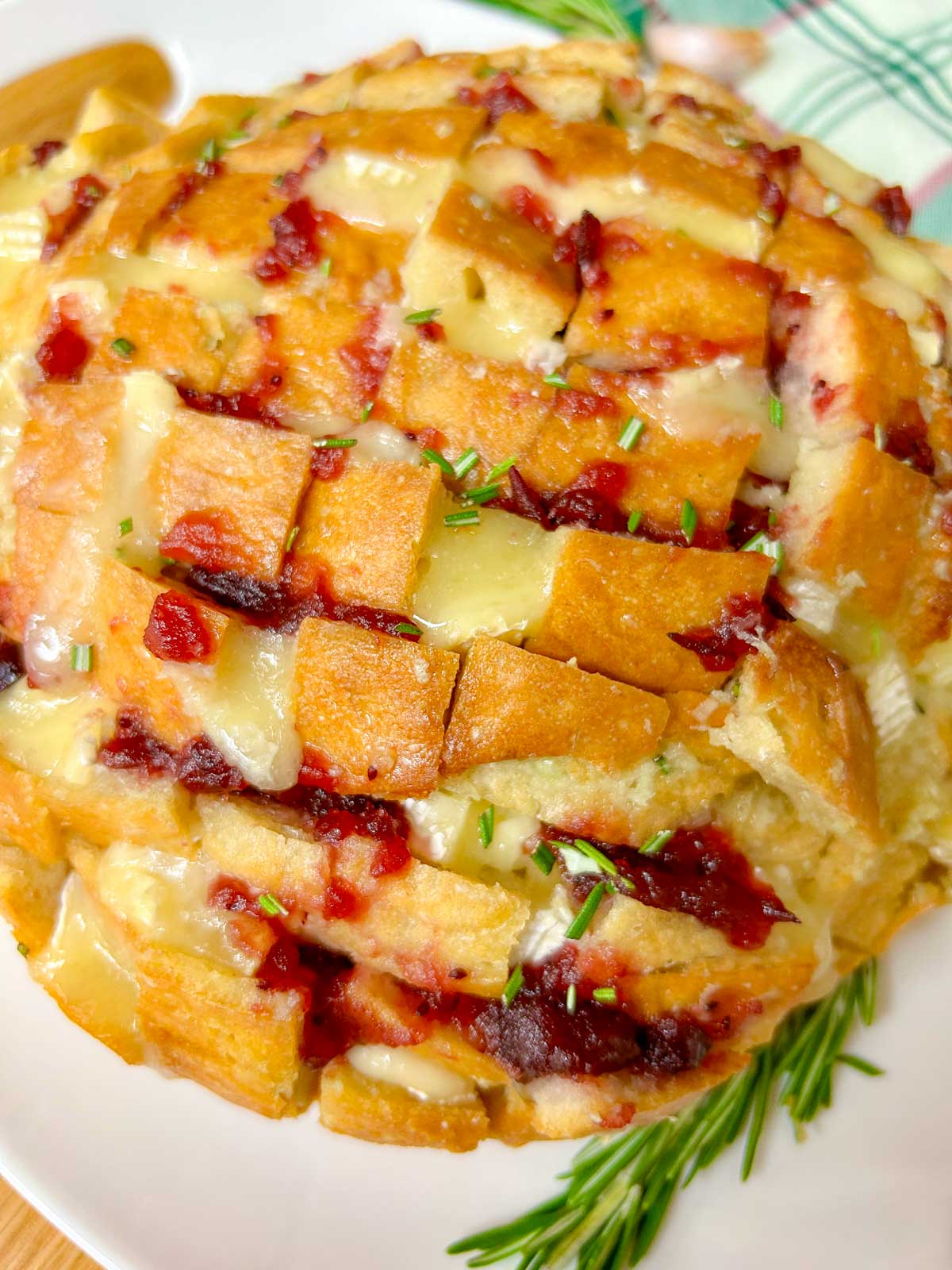 a loaf of cranberry brie pull apart garlic bread it on a white platter and garnished with rosemary