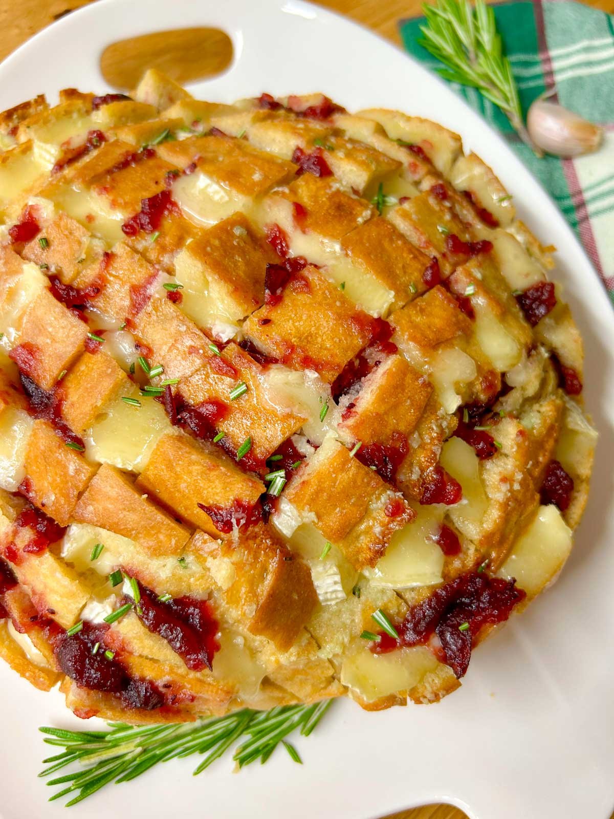 a loaf of cranberry brie pull apart garlic bread it on a white platter and garnished with rosemary