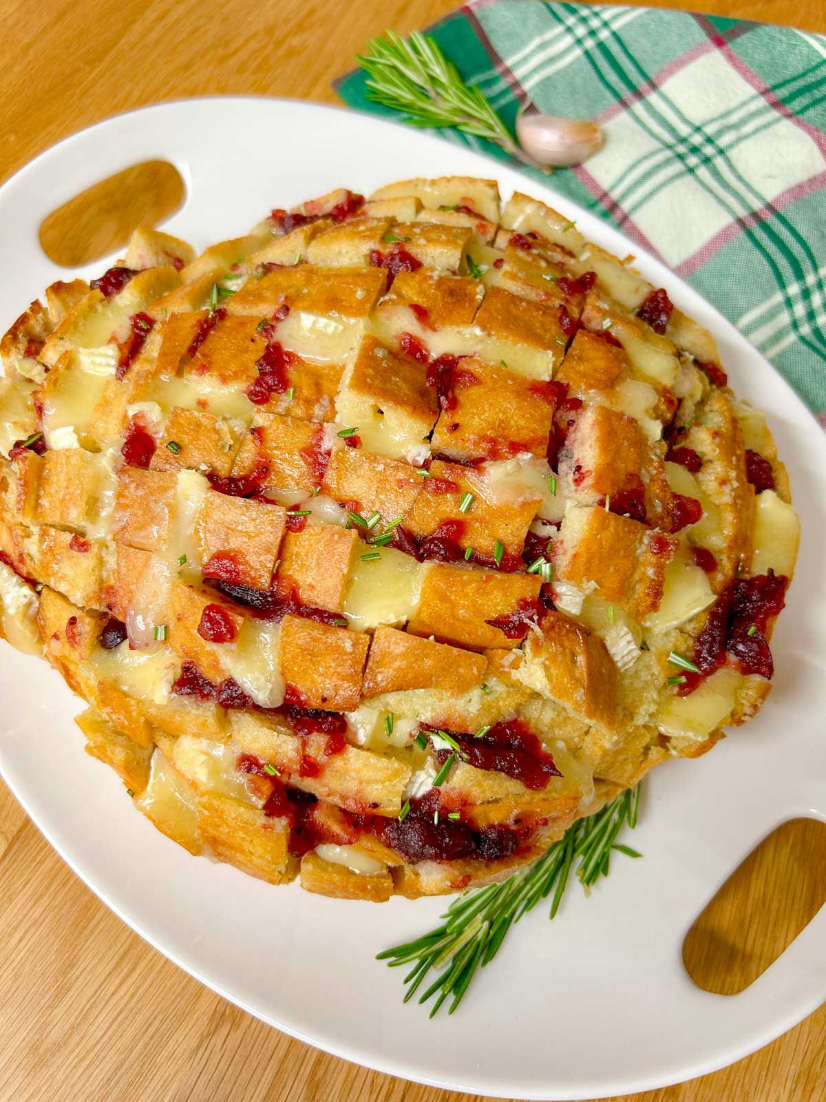 a loaf of cranberry brie pull apart garlic bread it on a white platter and garnished with rosemary