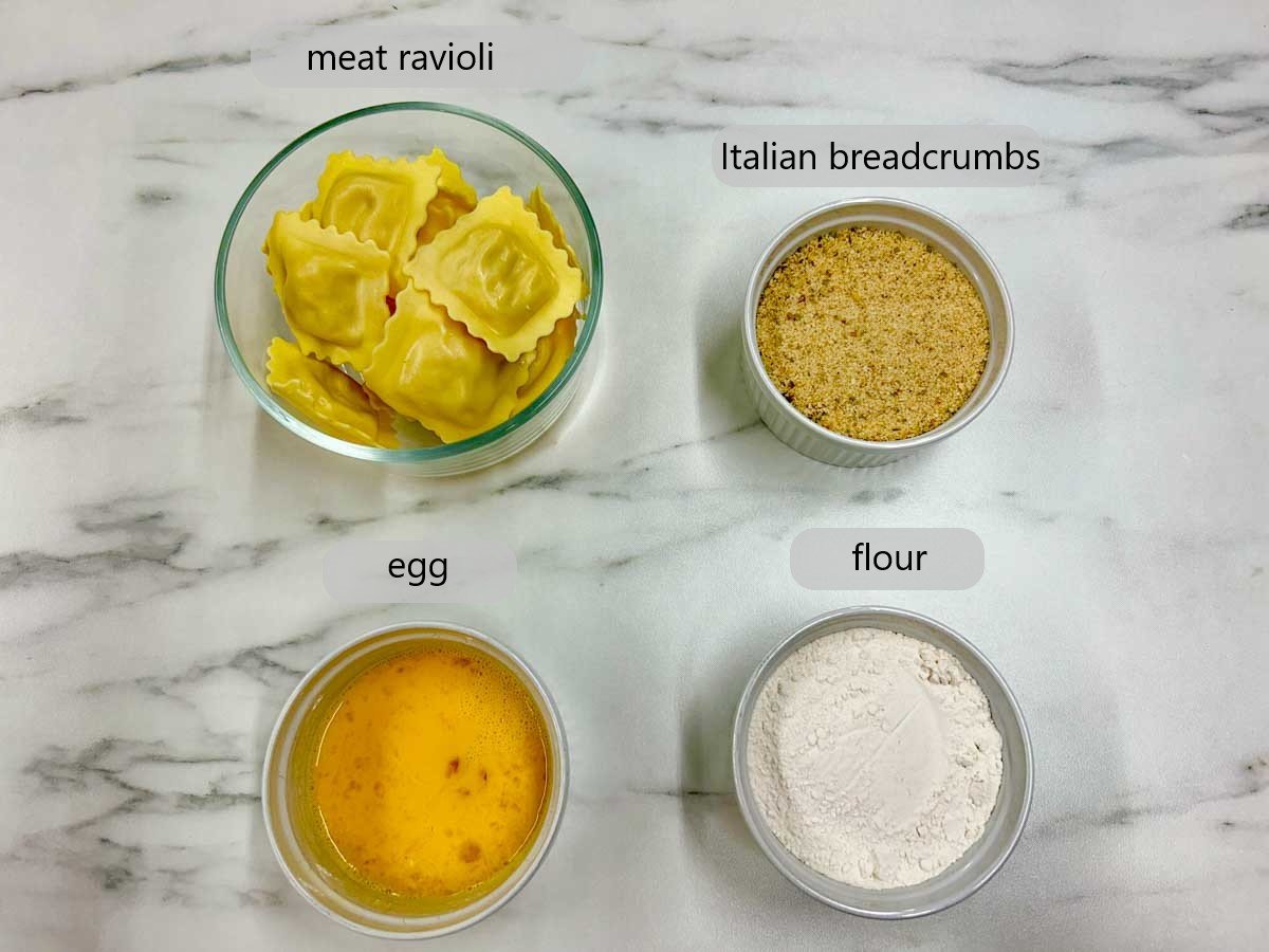 a kitchen counter with bowls and the ingredients to make olive garden toasted ravioli with the text labels reading meat ravioli, Italian breadcrumbs, egg, and flour