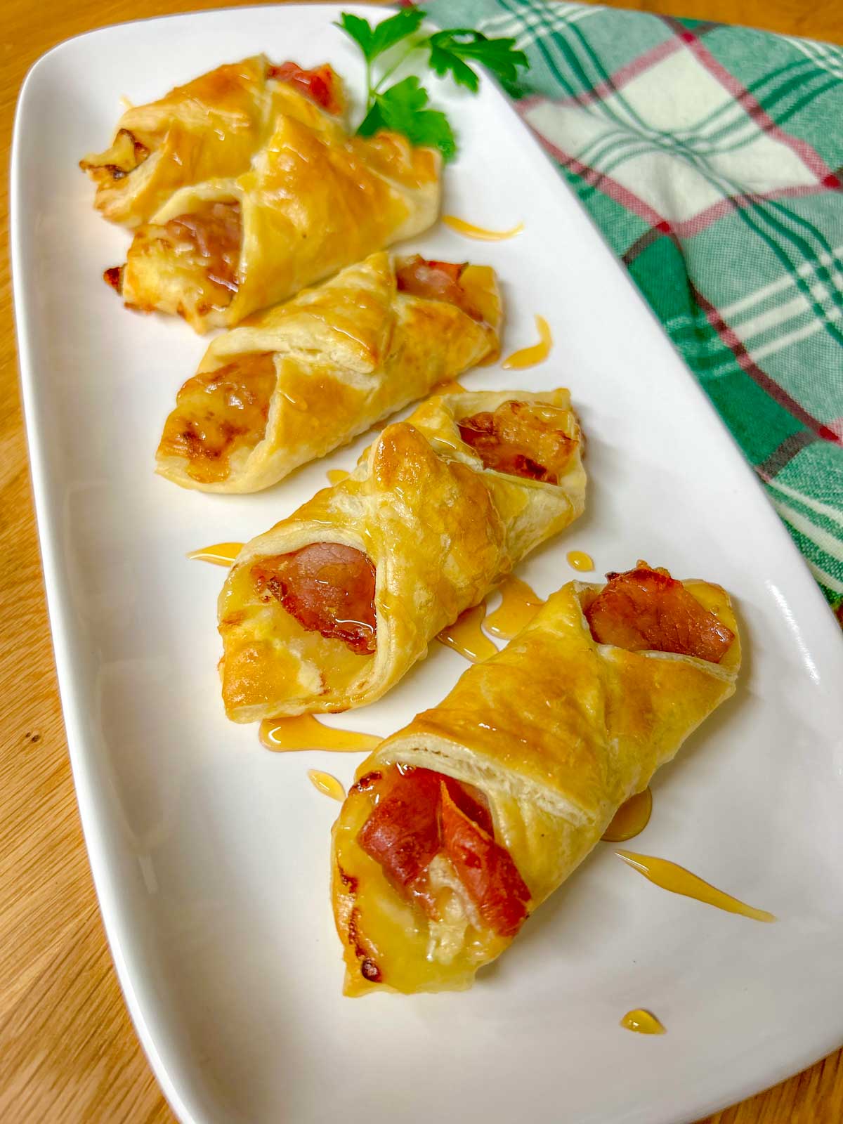 a white platter had prosciutto wrapped brie and fig puffs and they are drizzled with honey