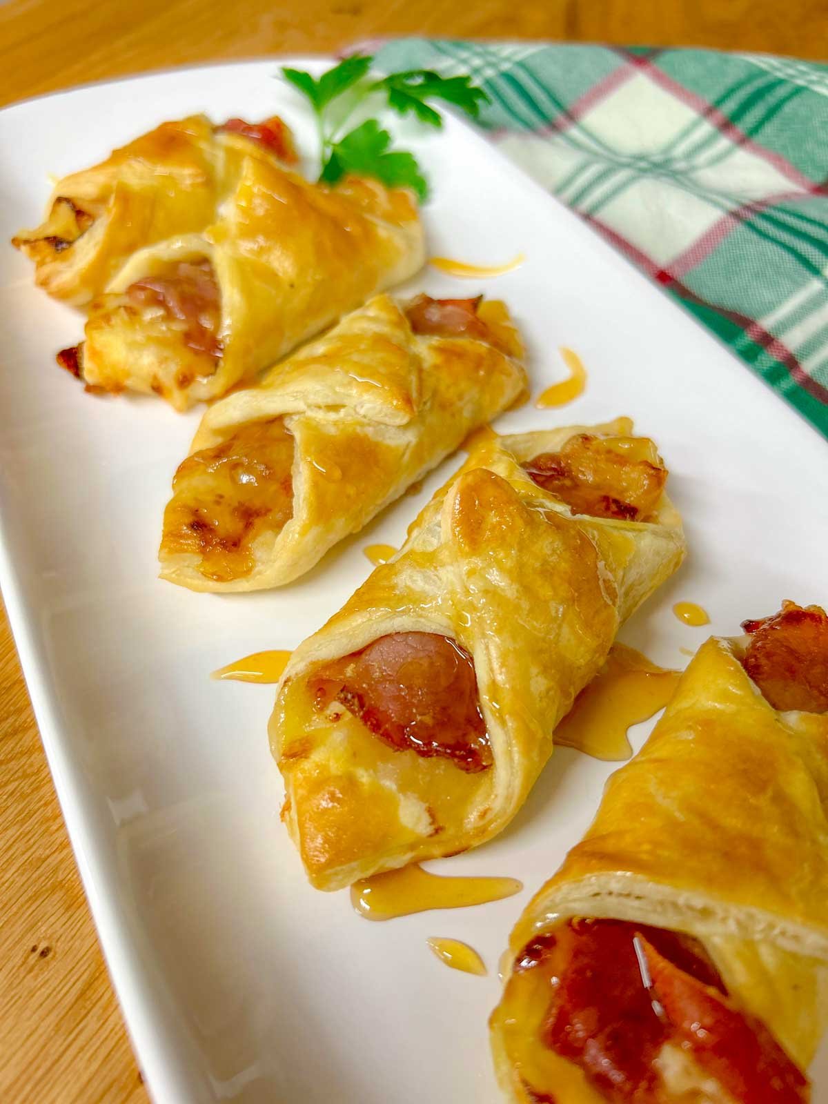 a white platter had prosciutto wrapped brie and fig puffs and they are drizzled with honey