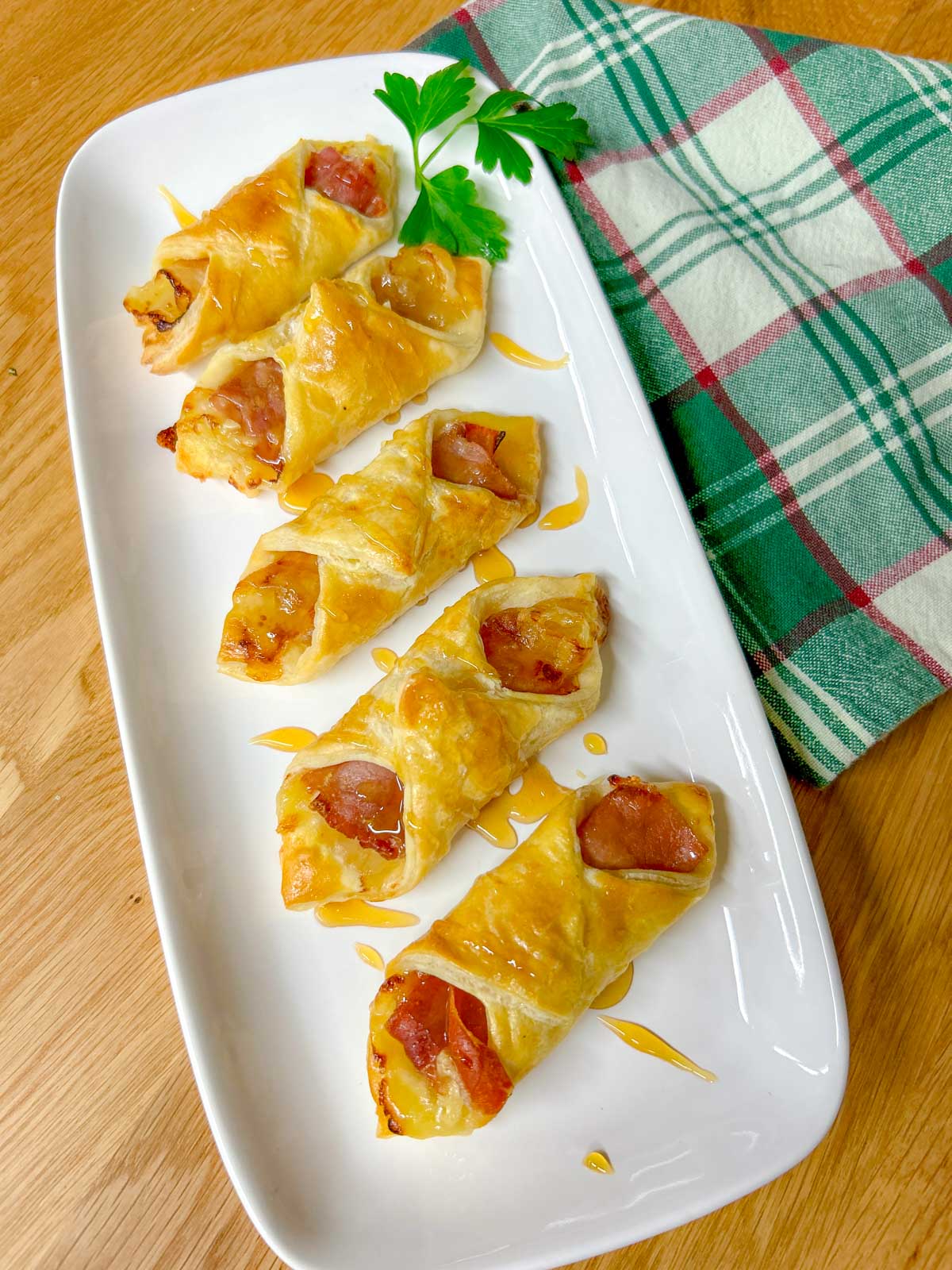 a white platter had prosciutto wrapped brie and fig puffs and they are drizzled with honey