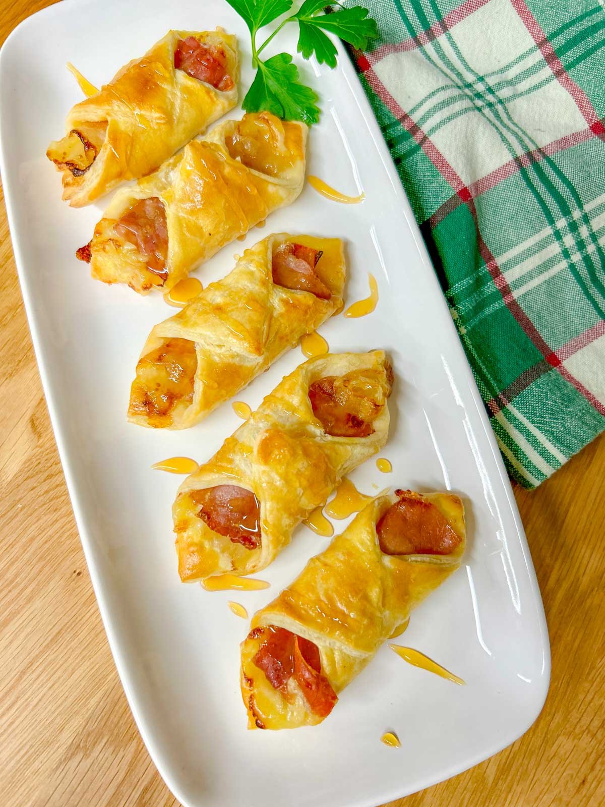 a white platter had prosciutto wrapped brie and fig puffs and they are drizzled with honey