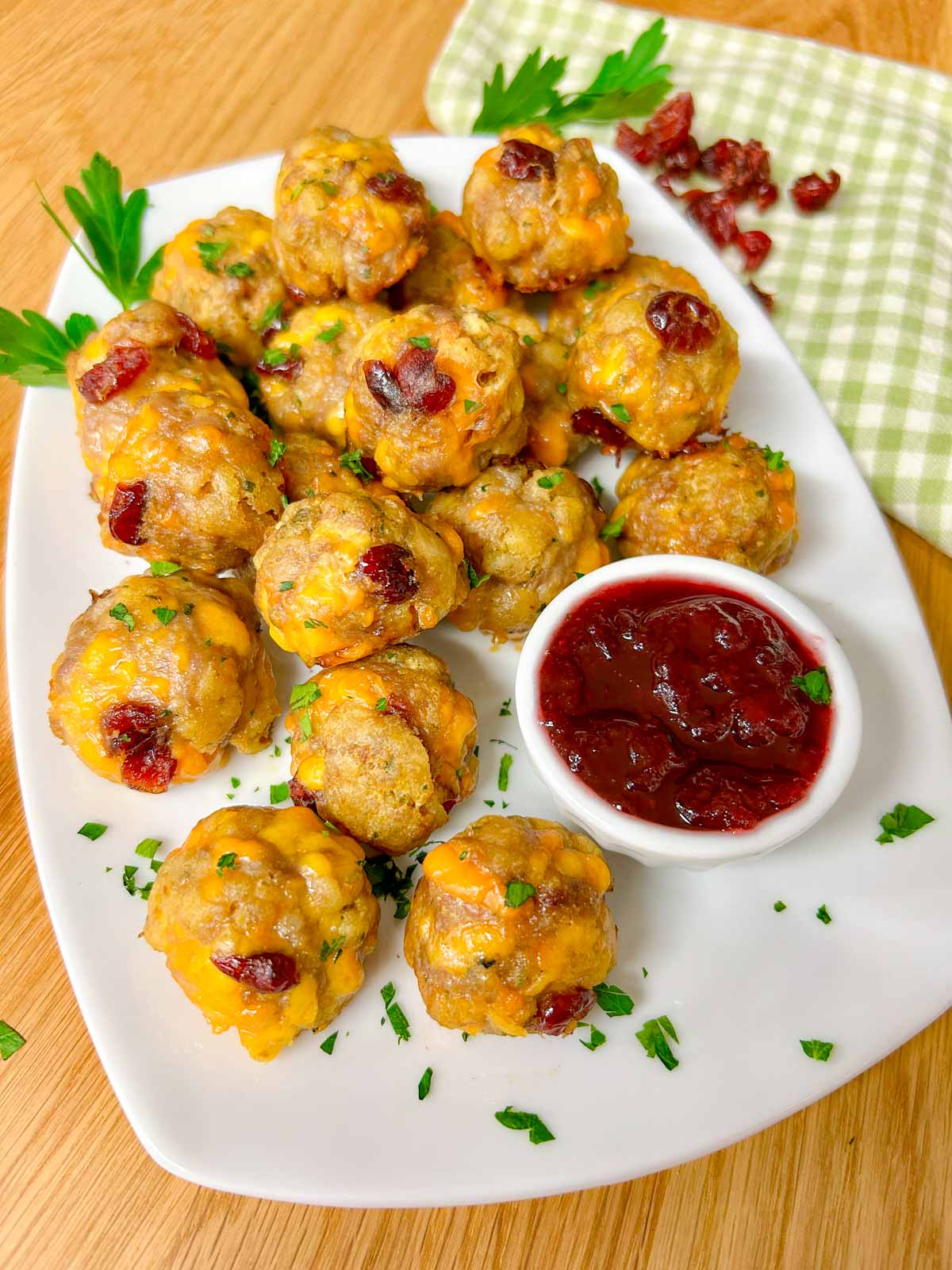 a white plate has sausage stuffing balls on top with a side dish of cranberry sauce for dipping