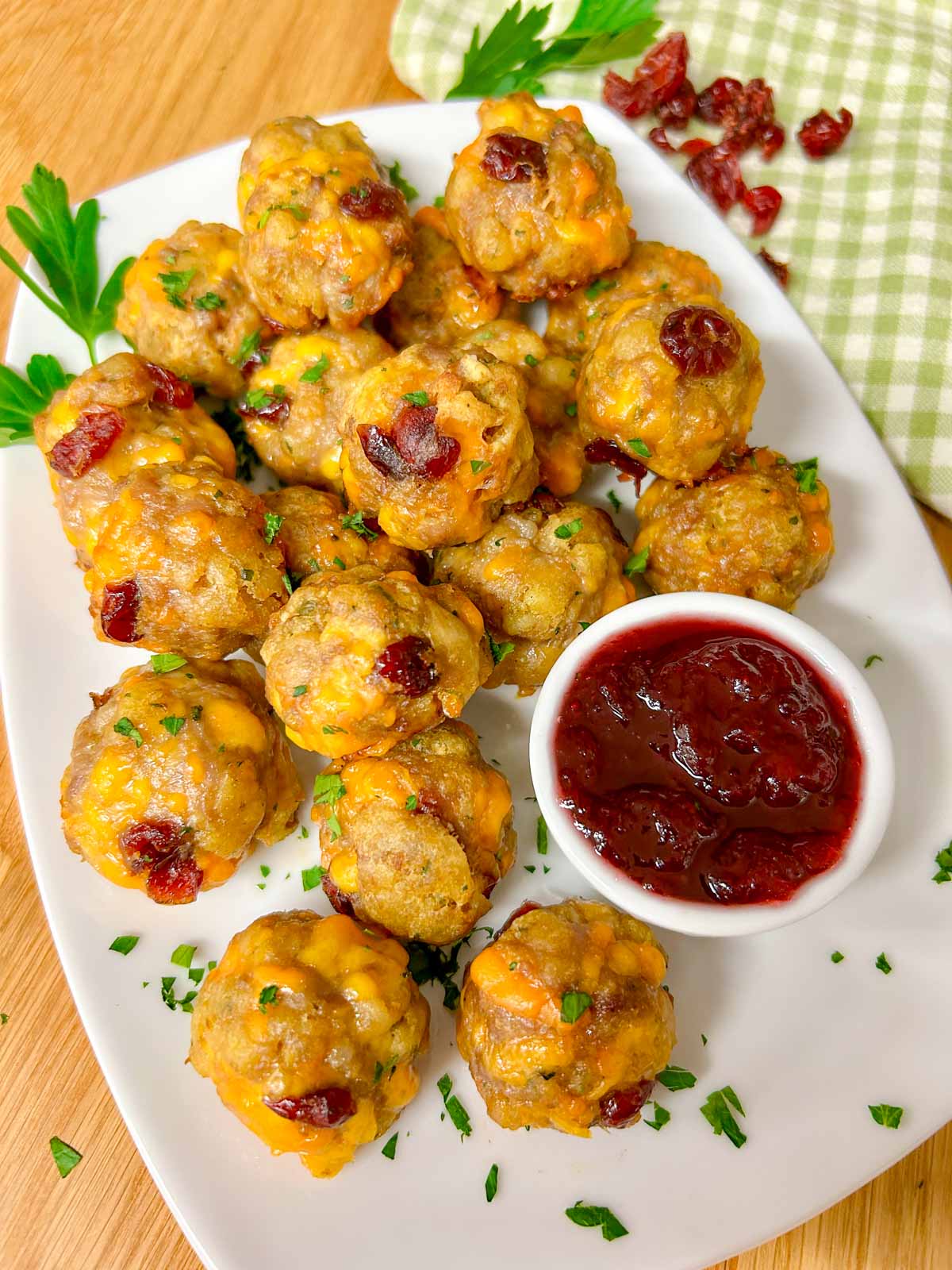 a white plate has sausage stuffing balls on top with a side dish of cranberry sauce for dipping