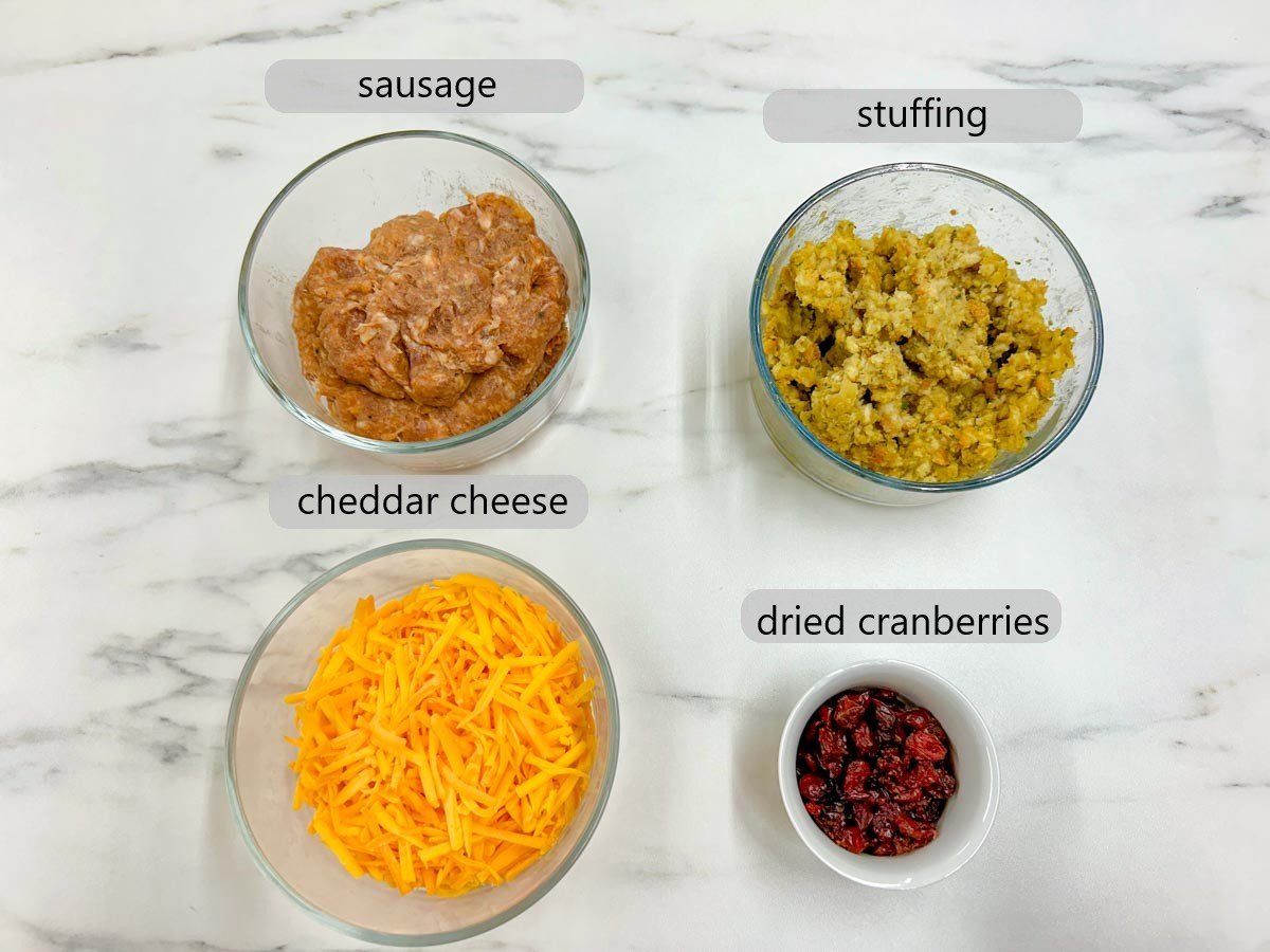 a counter top with bowls with the ingredients to make stuffing sausage balls - sausage, stuffing, cheddar cheese, and dried cranberries