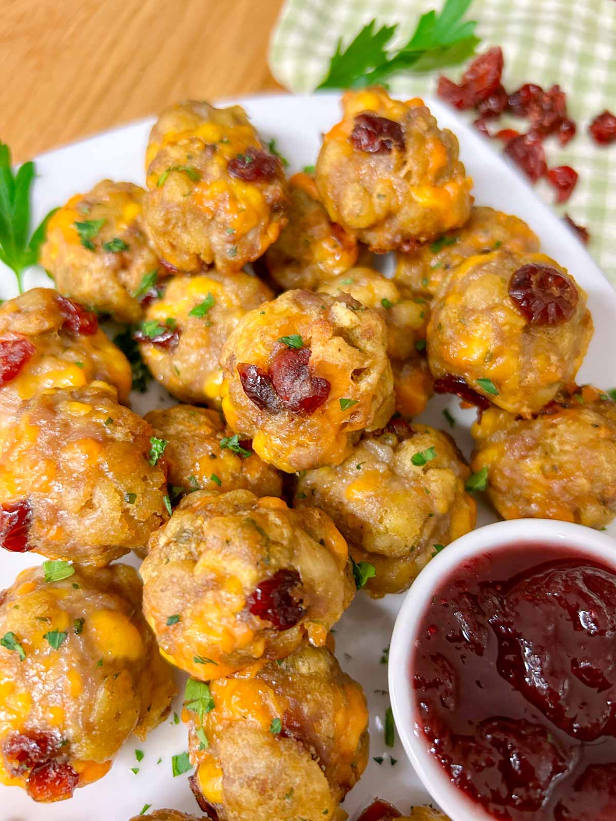 a white plate has sausage stuffing balls on top with a side dish of cranberry sauce for dipping