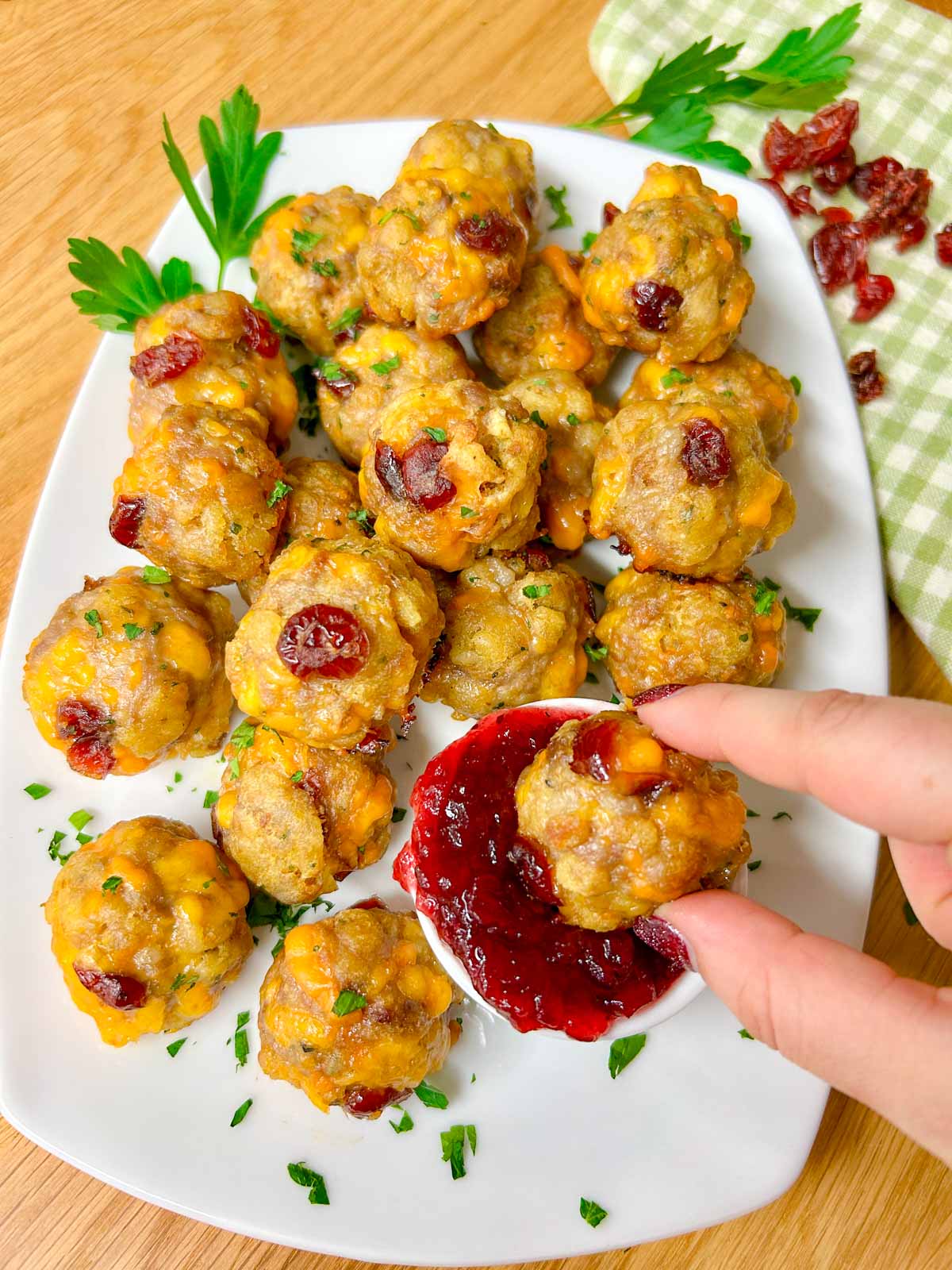 a white plate has sausage stuffing balls on top with a side dish of cranberry sauce for dipping, one is dipped in the sauce