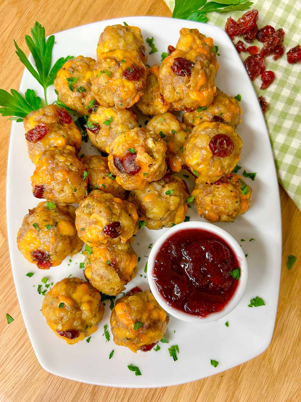 a white plate has sausage stuffing balls on top with a side dish of cranberry sauce for dipping