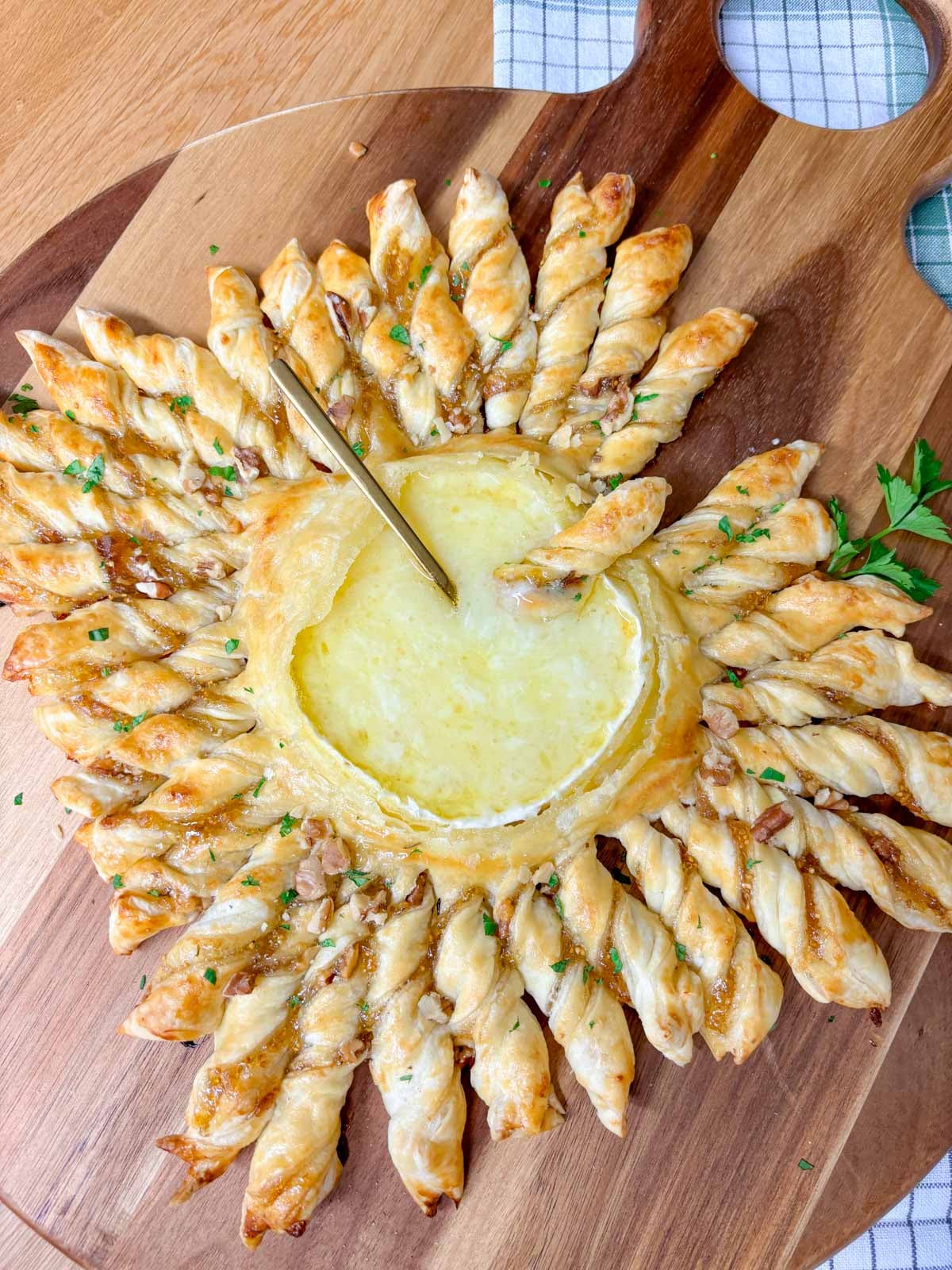 a wood serving board has a twisted pastry ring with a dipping bowl of brie in the centre