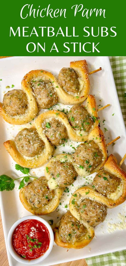 a white plate has chicken parmesan meatball subs on a stick with a side of marinara sauce to dip. garnished with parsley and parmesan cheese.