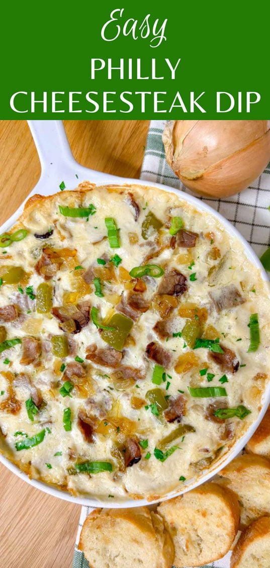 a white baking dish is filled with Philly cheesesteak dip. peppers, onions, roast beef and green onions garnish the dip