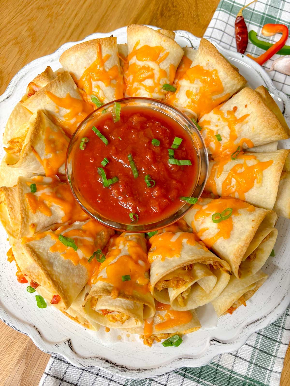 a white platter has a chicken quesadilla ring on it garnished with green onions and a bowl of salsa in the middle.