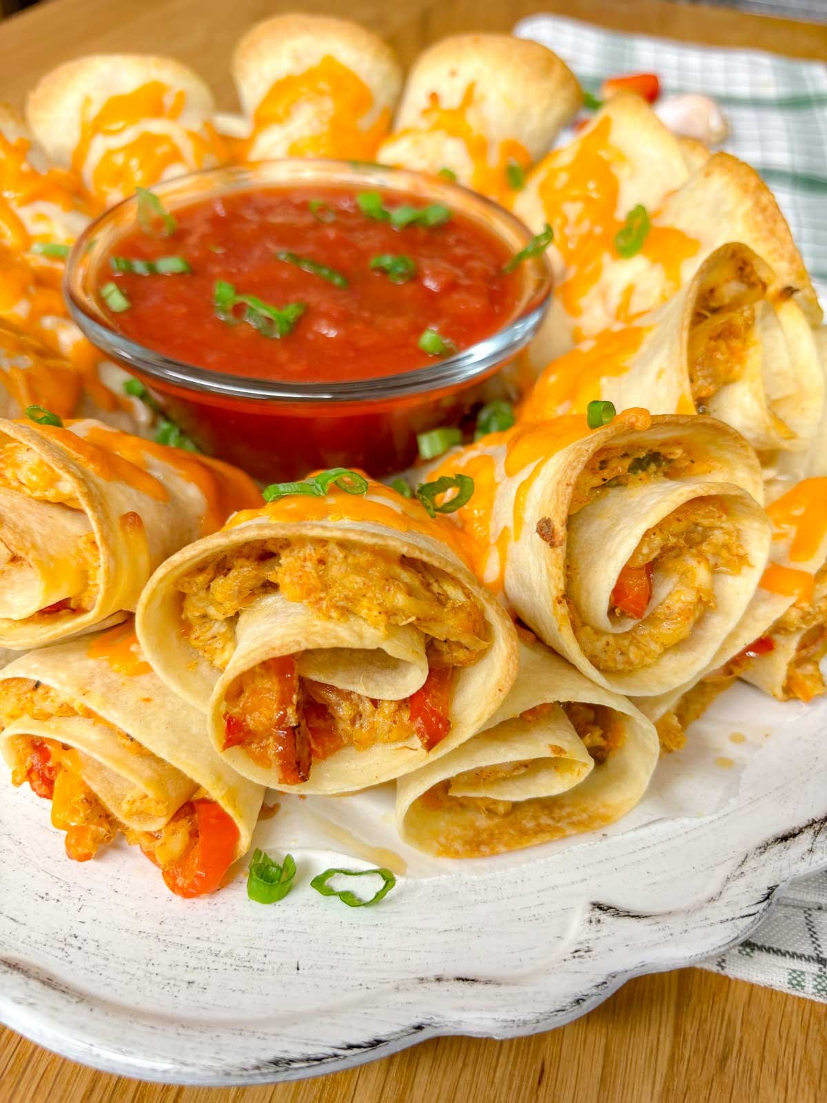 a white platter has a chicken quesadilla ring on it garnished with green onions and a bowl of salsa in the middle.