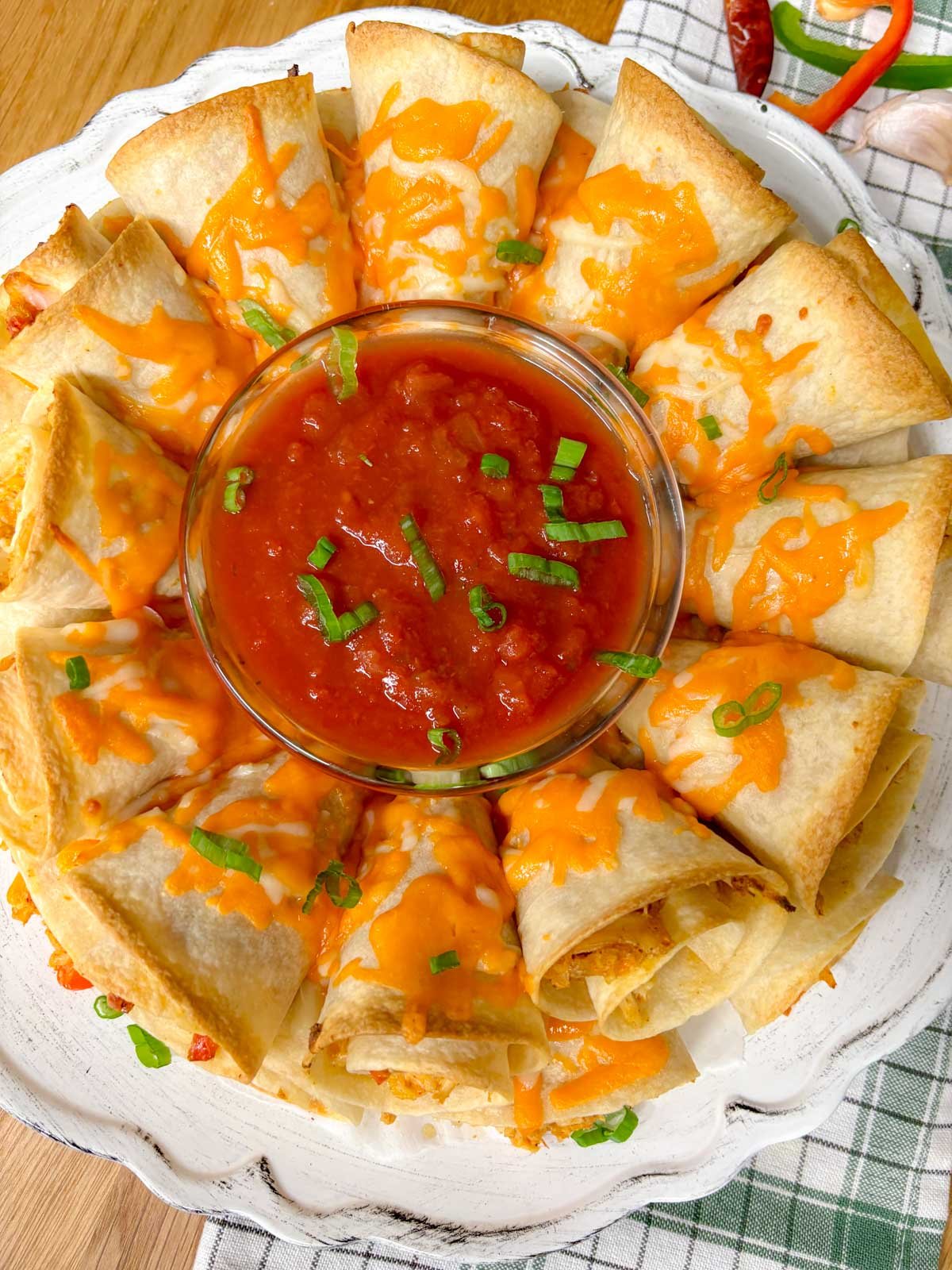 a white platter has a chicken quesadilla ring on it garnished with green onions and a bowl of salsa in the middle.